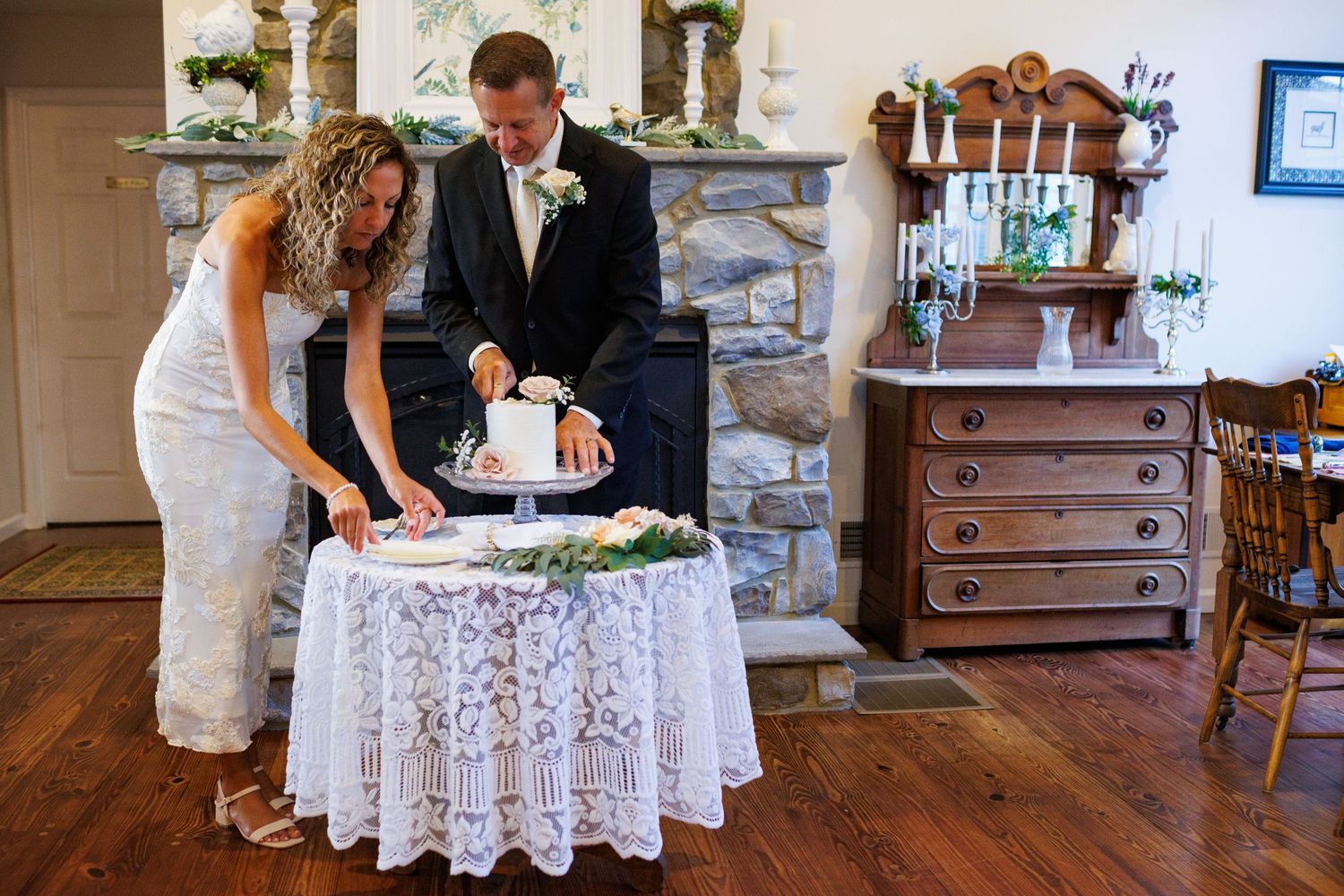 Bride and groom cutting their white wedding cake beside a stone fireplace at their reception.