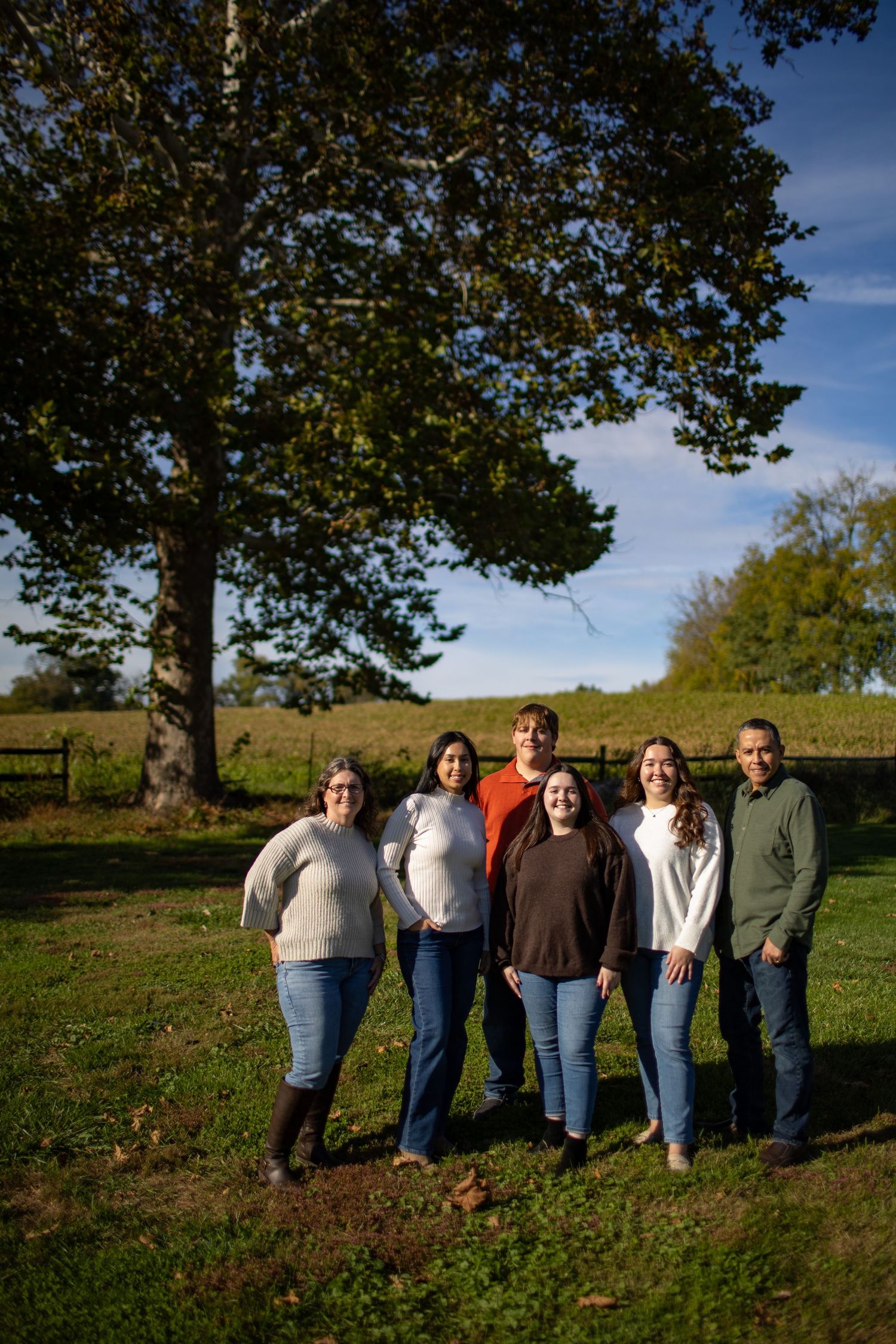A group of people standing together in a grassy field on a sunny autumn day with trees in the background.