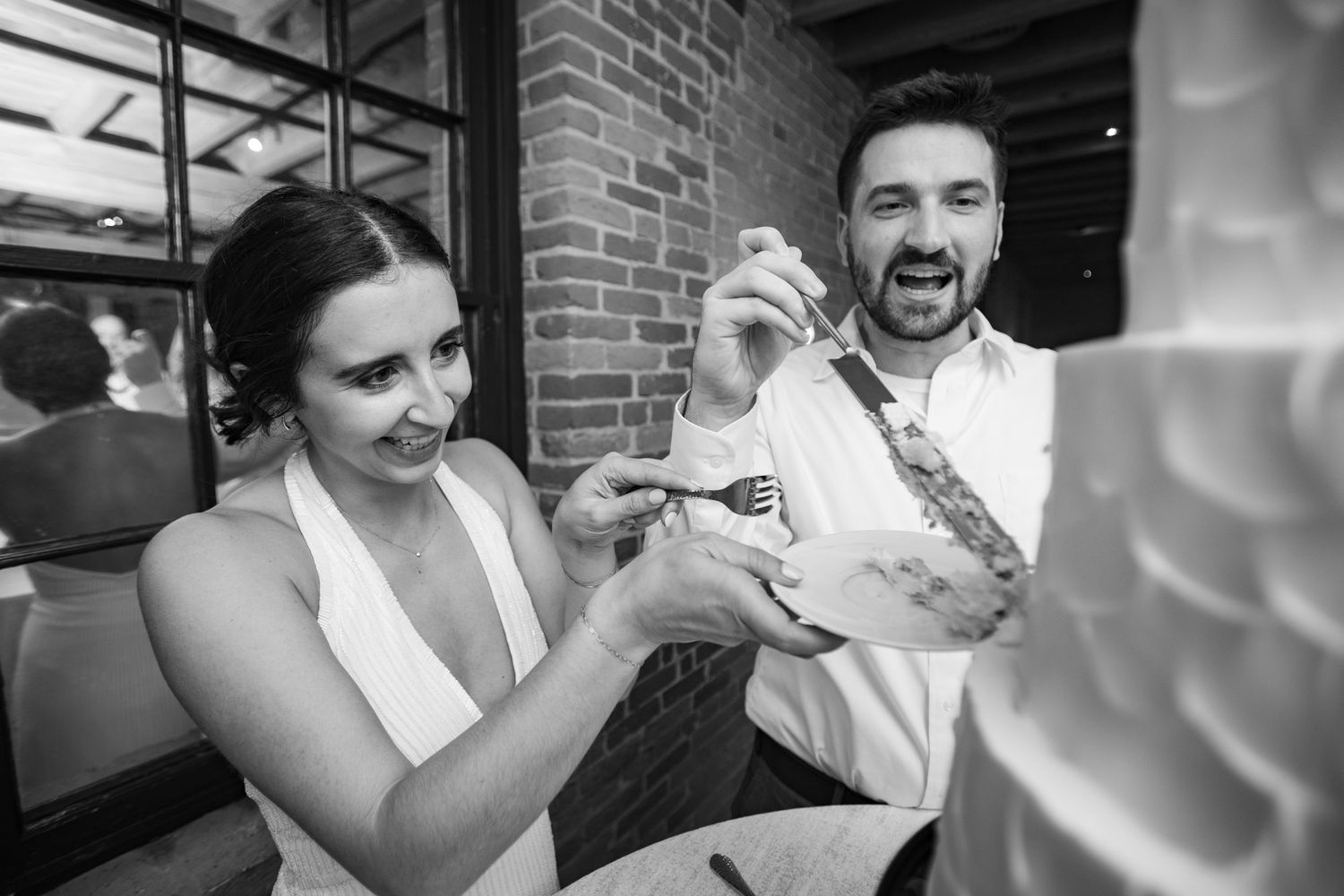Black and white photo of a bride and groom cutting their wedding cake together, smiling joyfully.