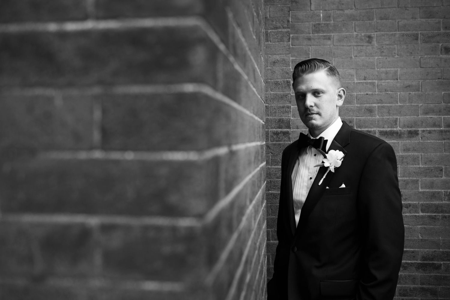 Black and white portrait against a brick wall with dramatic lighting.