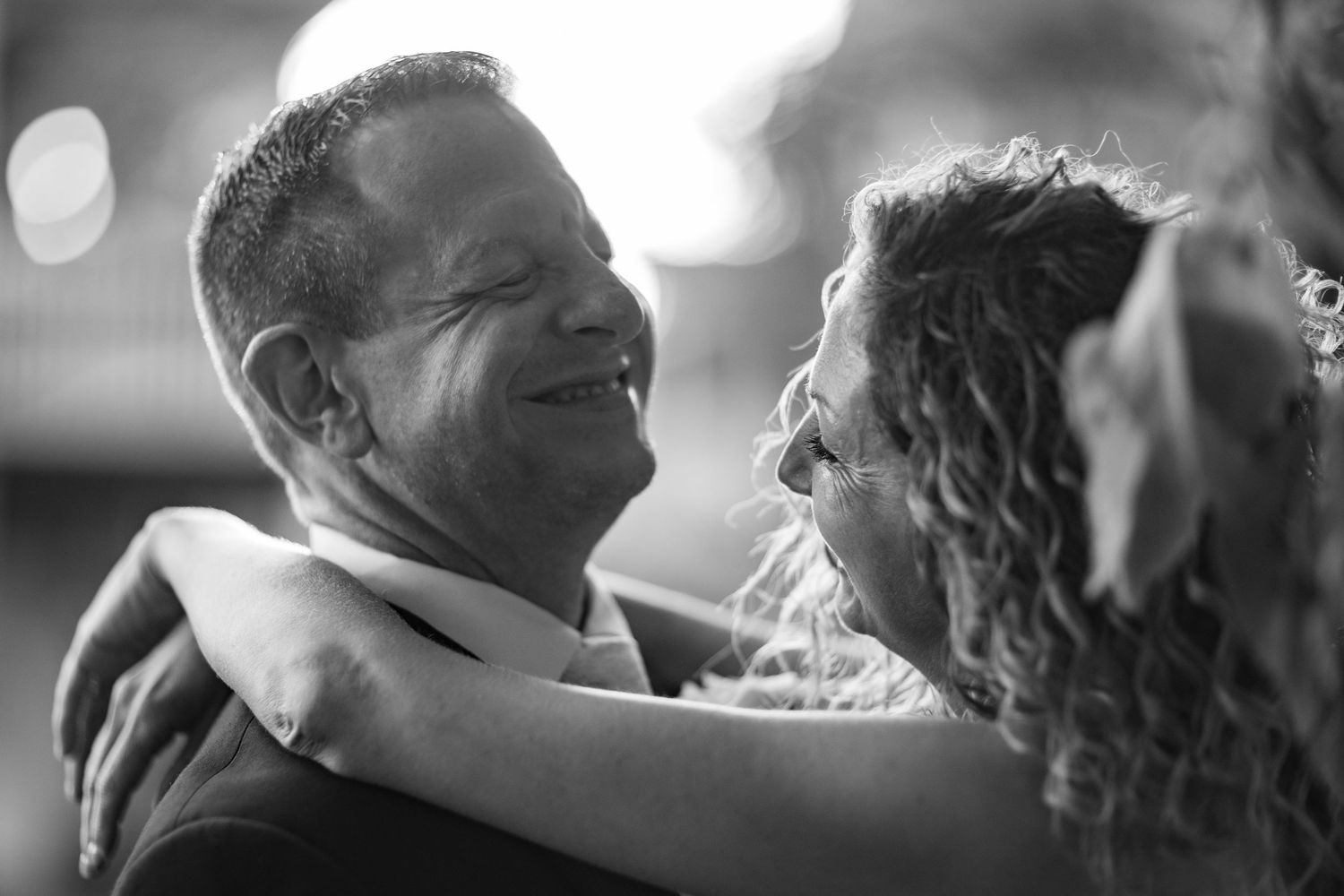 Black and white photo of a groom smiling joyfully at his bride during their first dance.