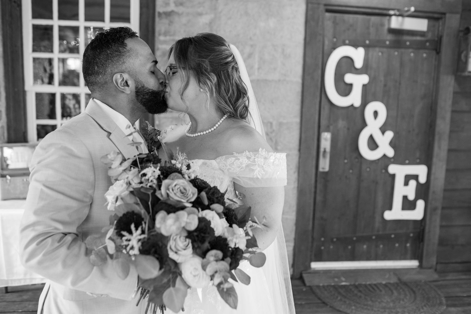 Newlyweds sharing a kiss in front of decorative G&E letters on their wedding day.