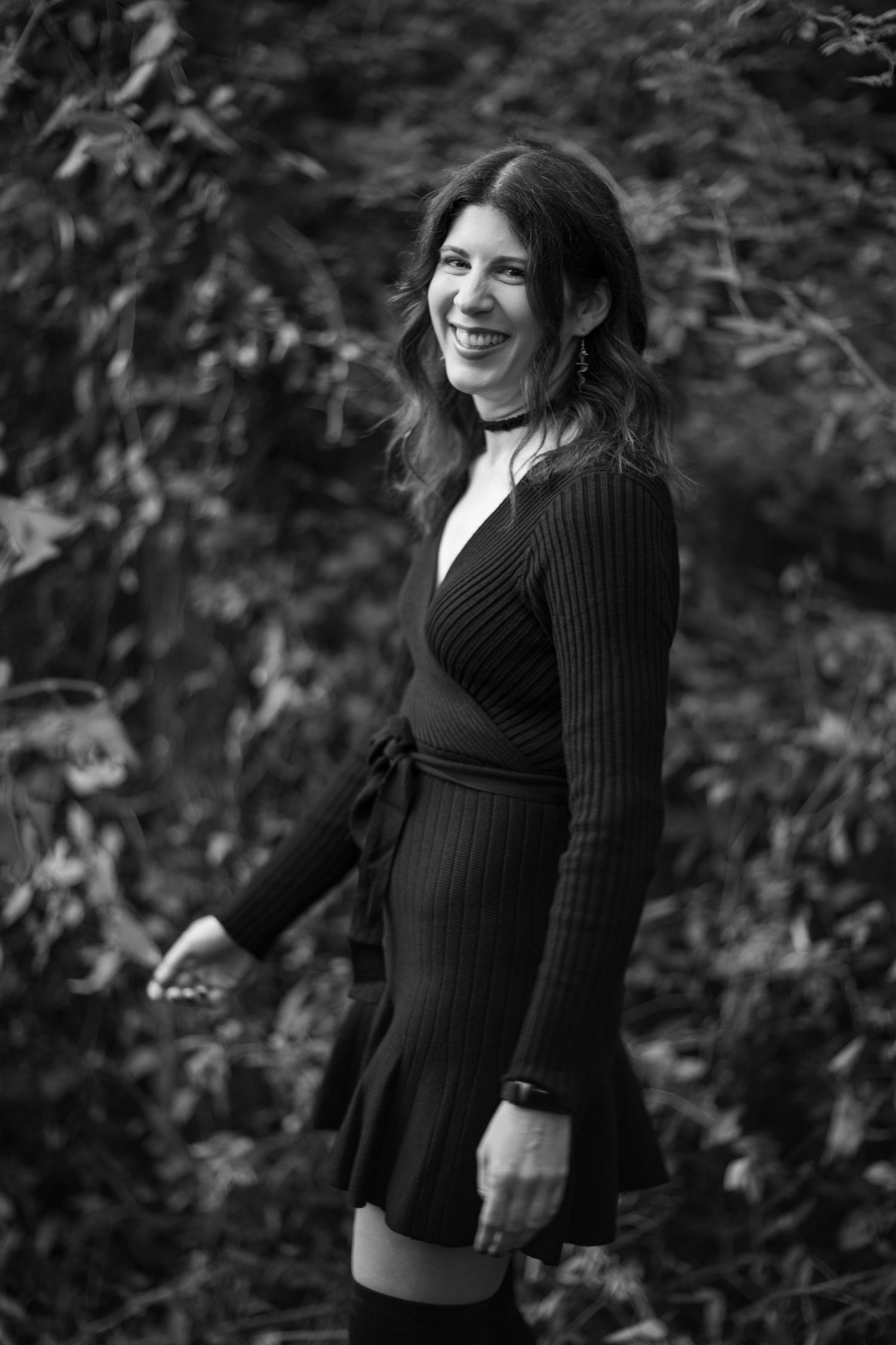 A series of black and white photos showing a person in a dark knit sweater smiling and posing against a blurred foliage background.