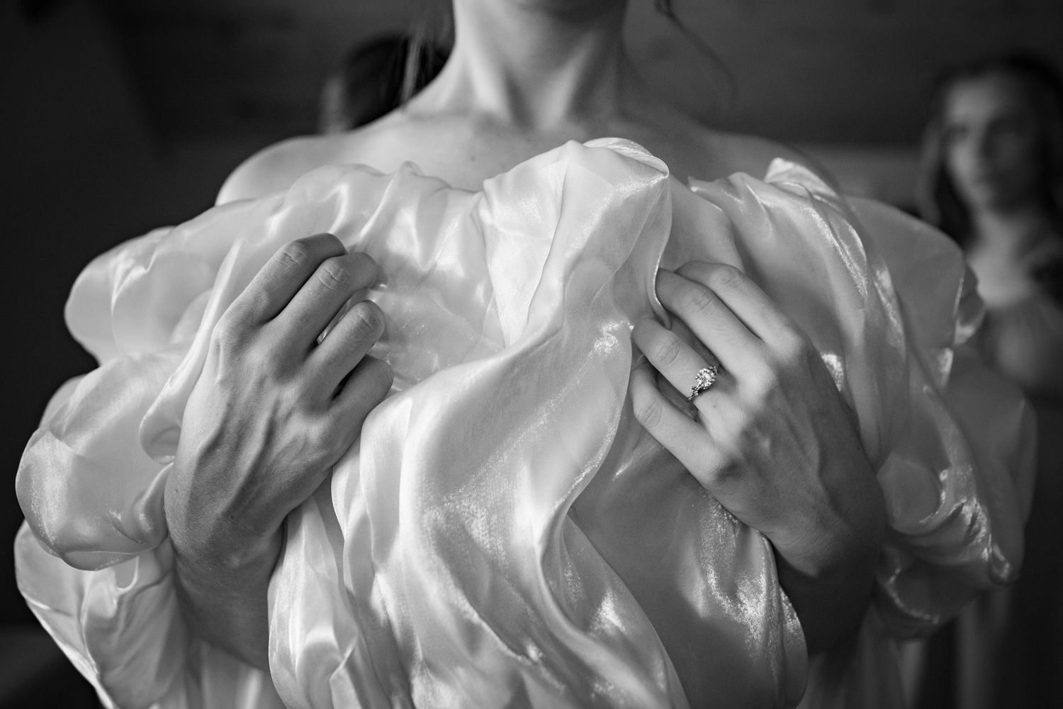 Close-up black and white photo of bride in ruffled off-shoulder wedding dress showing diamond engagement ring.