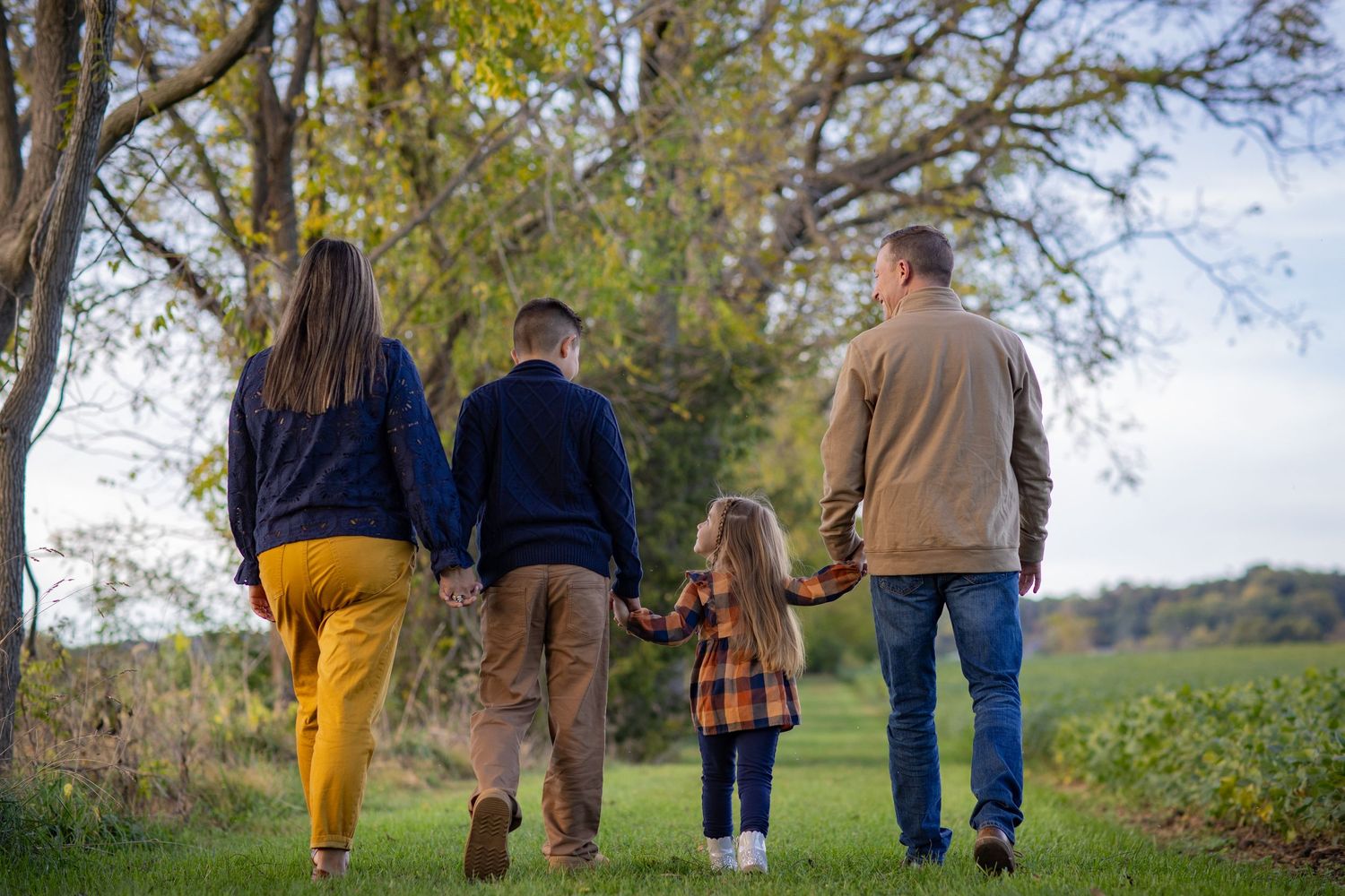 A group walks together through an autumn landscape with trees and grass on a sunny afternoon.