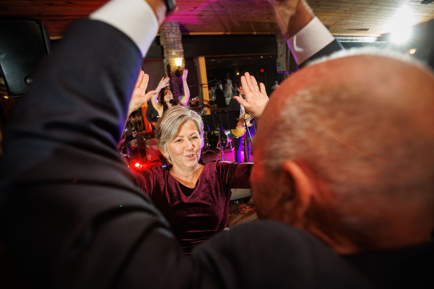 A woman in burgundy velvet dress high-fives guests at a lively wedding reception.