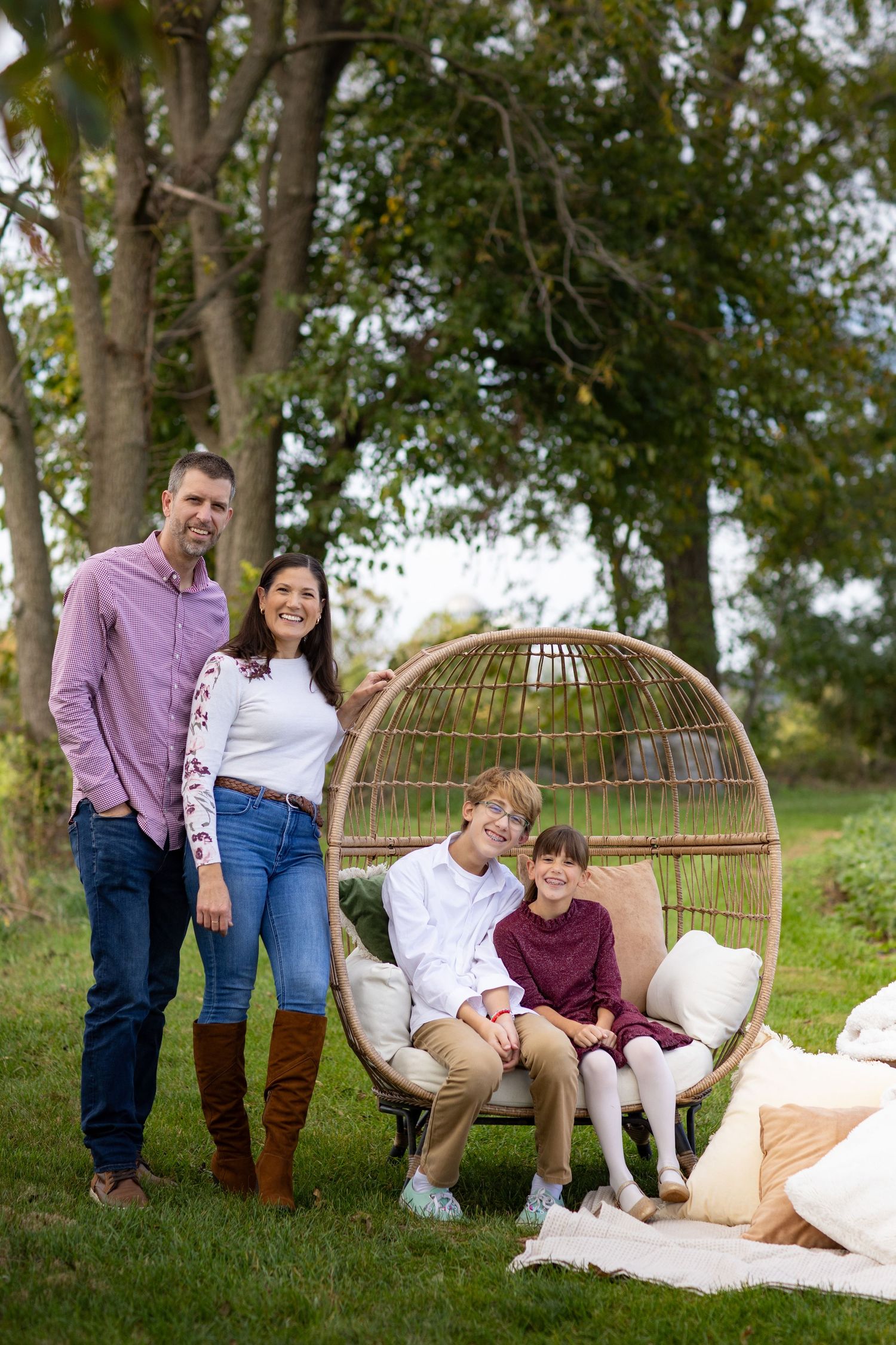 A family shares joyful moments together on a blanket outdoors with wicker furniture and natural greenery in the background.