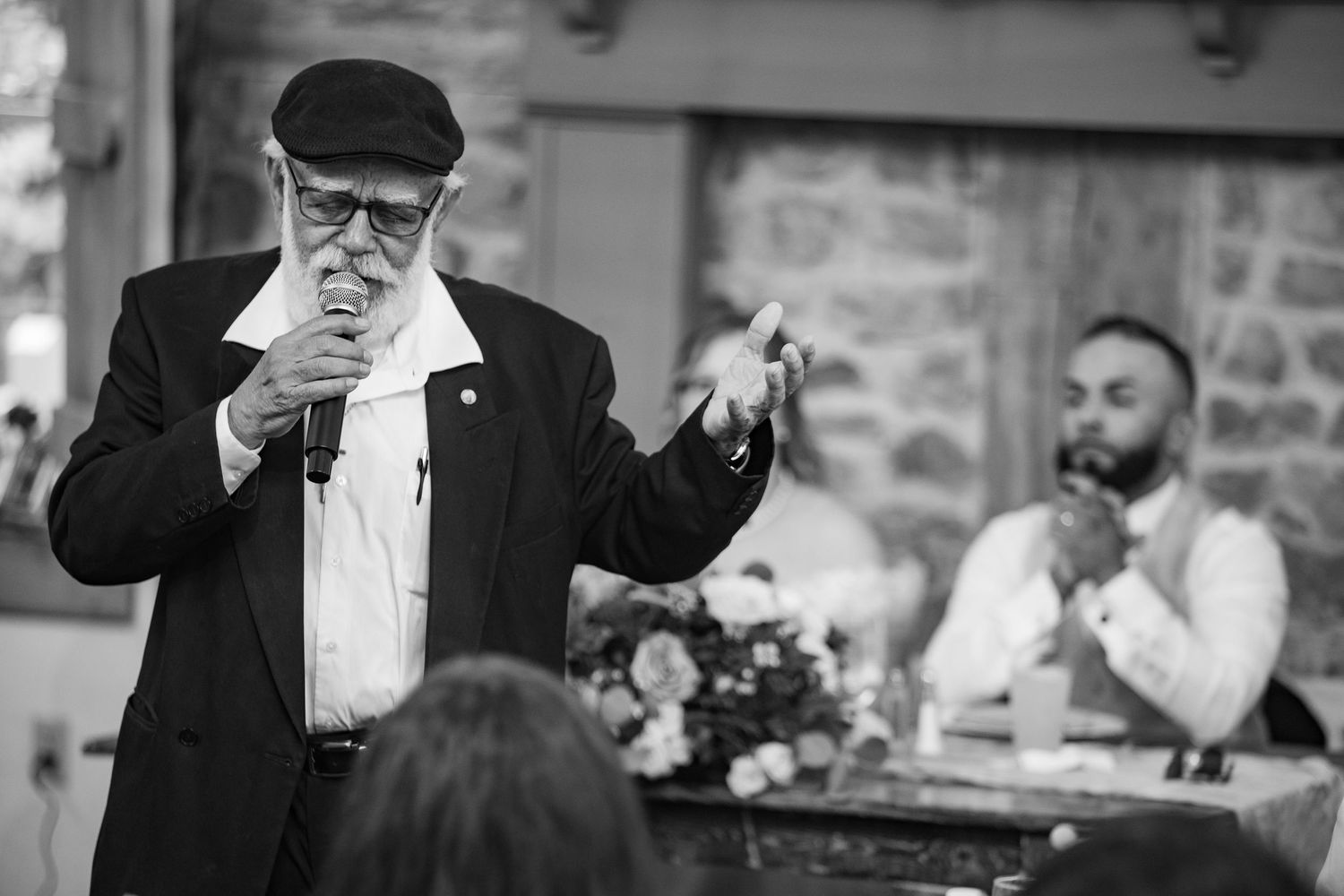 Elderly man giving a heartfelt wedding toast speech into a microphone in black and white.