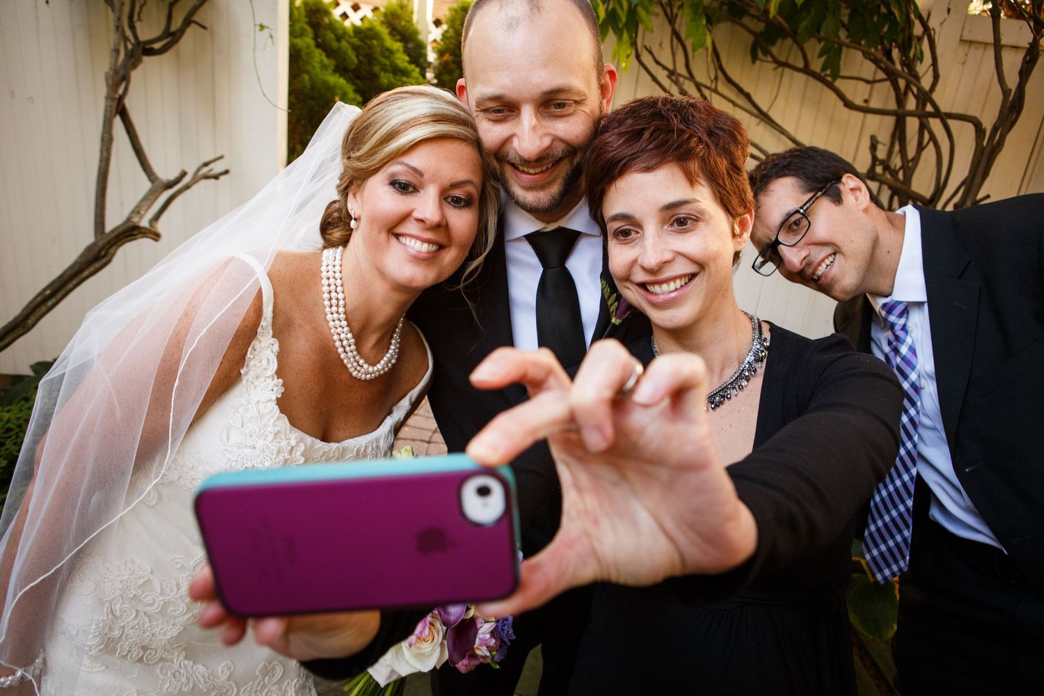 Group takes a fun selfie together at a wedding celebration outdoors with smiling faces gathered around a phone camera.