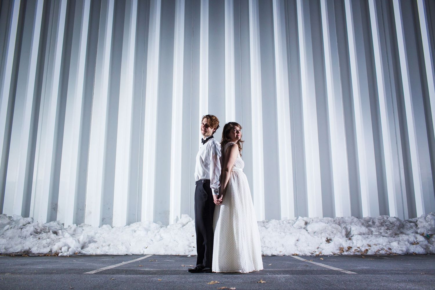 Bride and groom pose back-to-back against industrial striped metal wall.