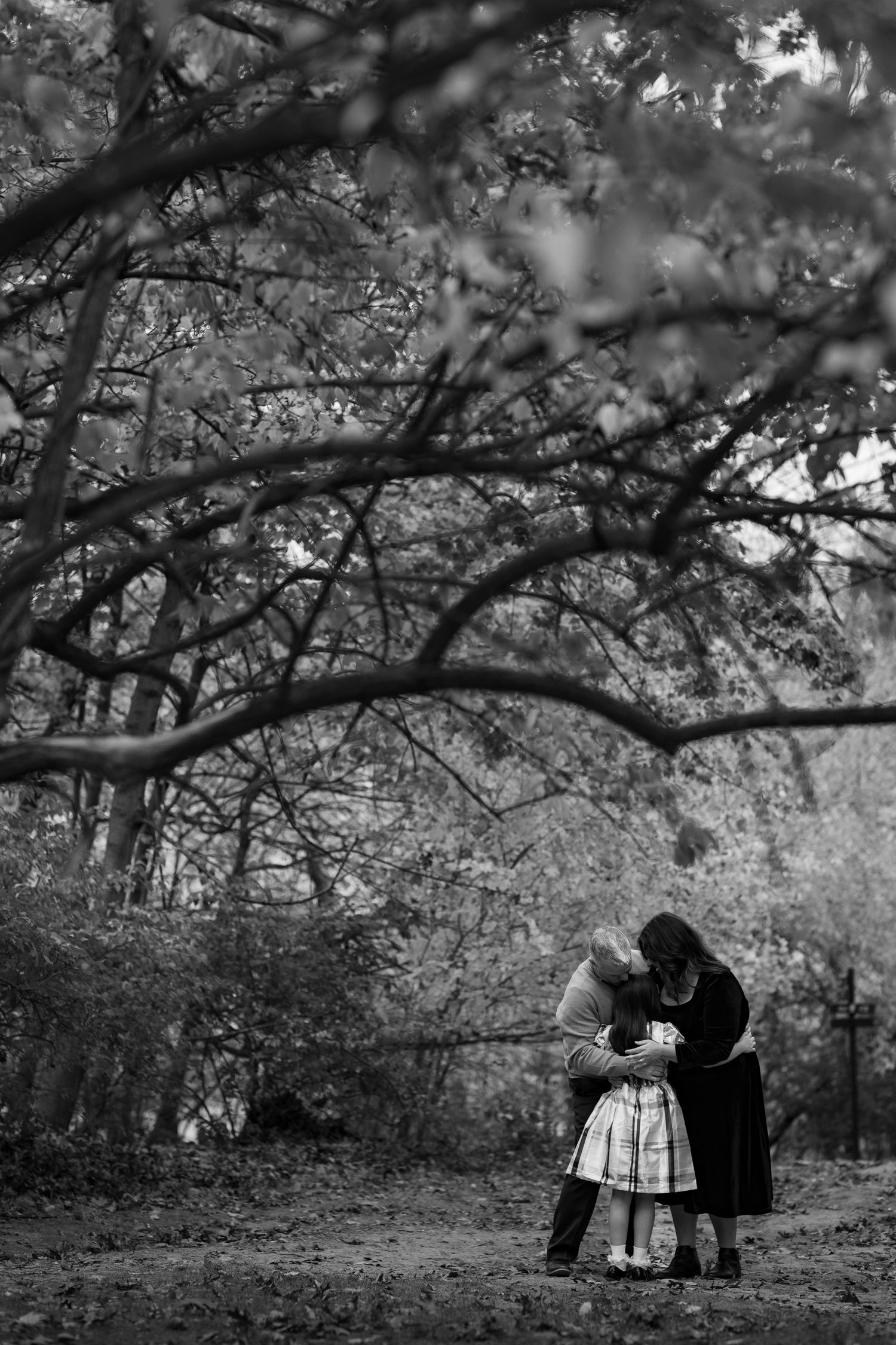 Black and white photo of a family sitting together under tree branches in a wooded setting.