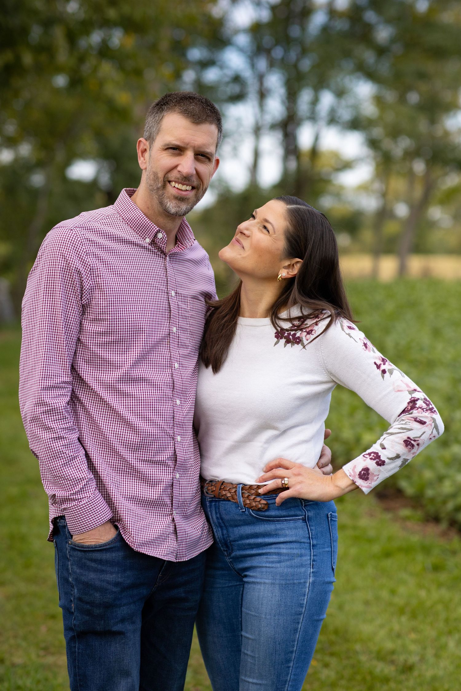 A couple in coordinating purple and white outfits share playful moments together outdoors during a photo session.
