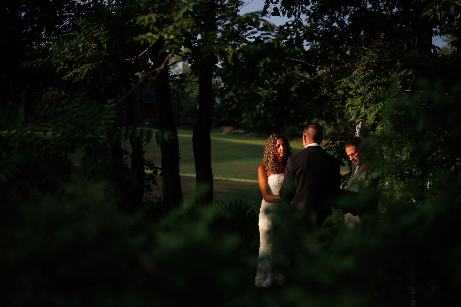 Couple exchanges vows in a lush forest clearing at dusk, with soft golden light illuminating their intimate outdoor wedding ceremony.