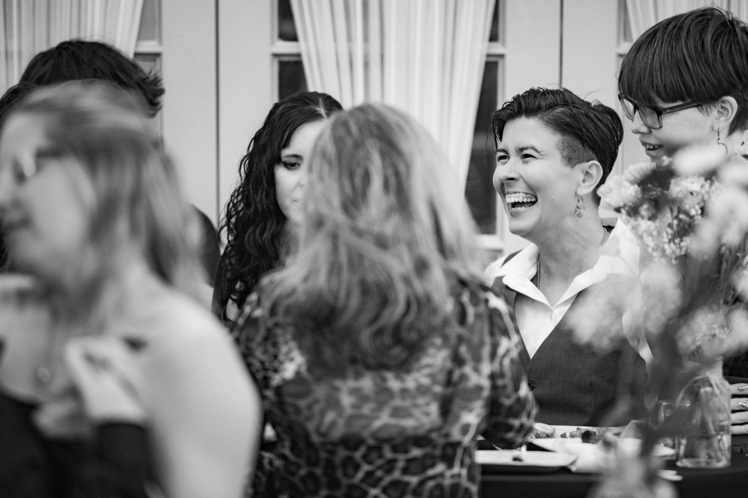 A candid black and white photo of guests laughing and socializing at an indoor event.