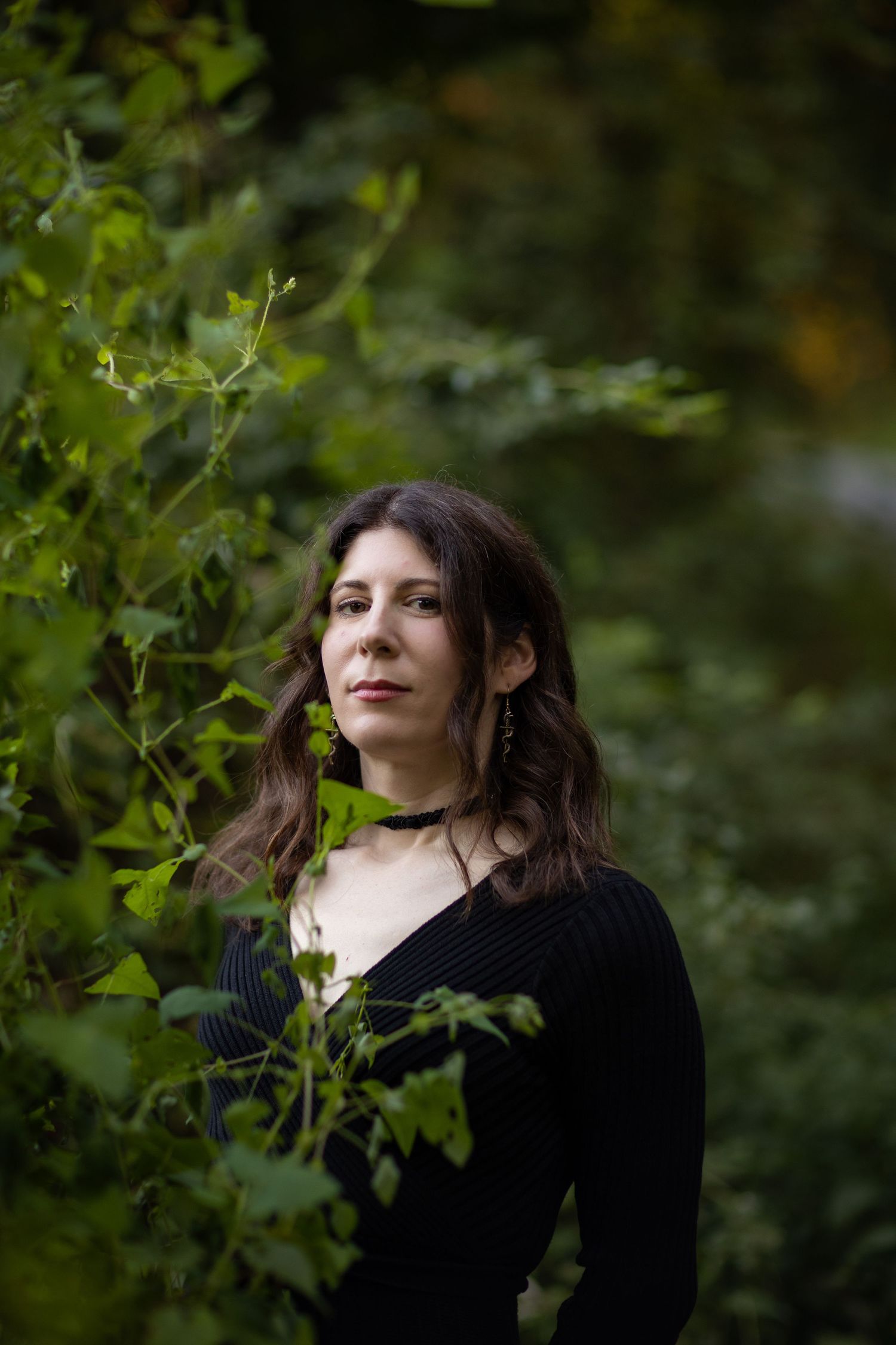 A woman in black is photographed in nature with trees and foliage in the background.