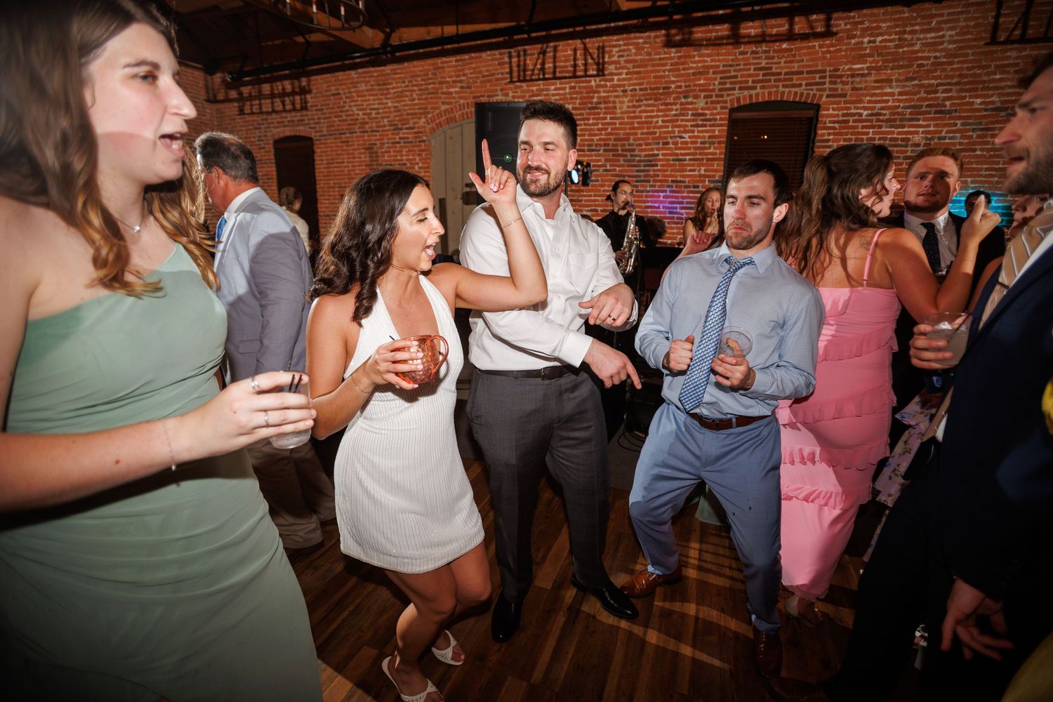 Guests dancing and celebrating at a wedding reception inside a rustic brick-walled venue.