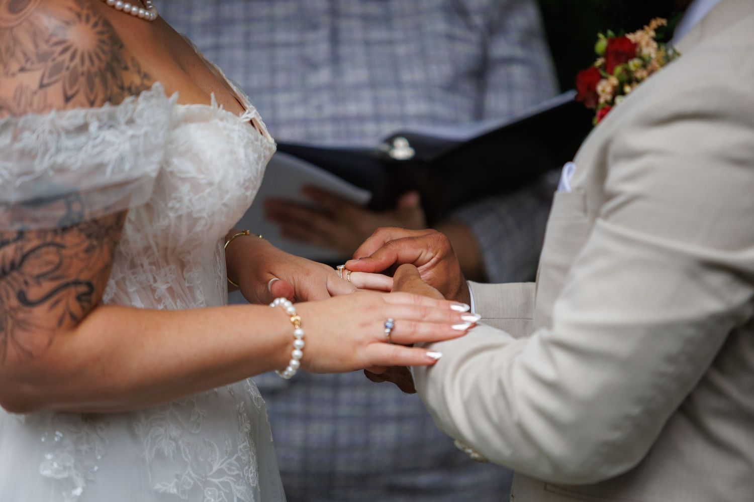Bride and groom exchanging rings during an outdoor wedding ceremony, bride wearing lace gown.