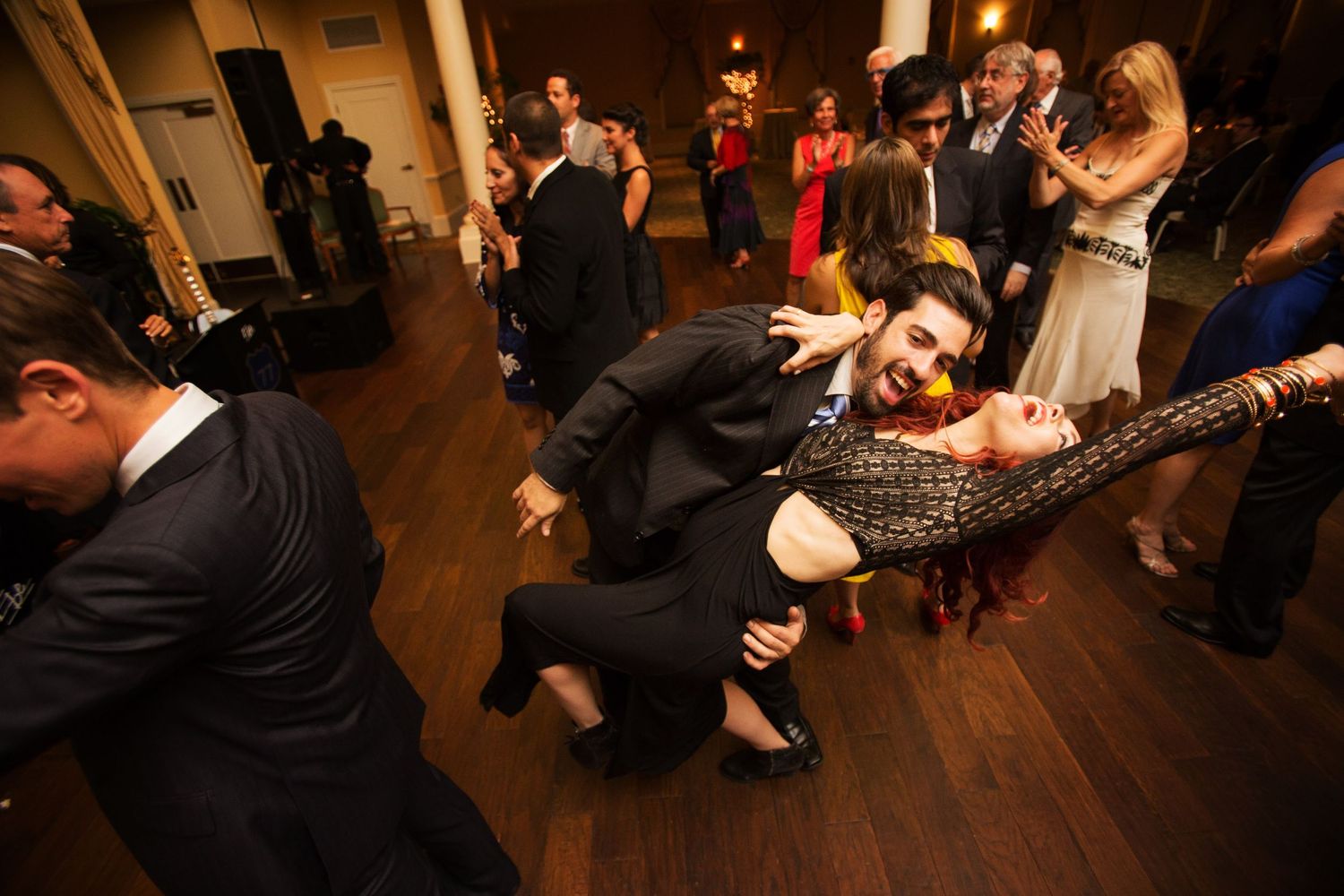 Party guests dance energetically on a wooden dance floor at an indoor celebration event.