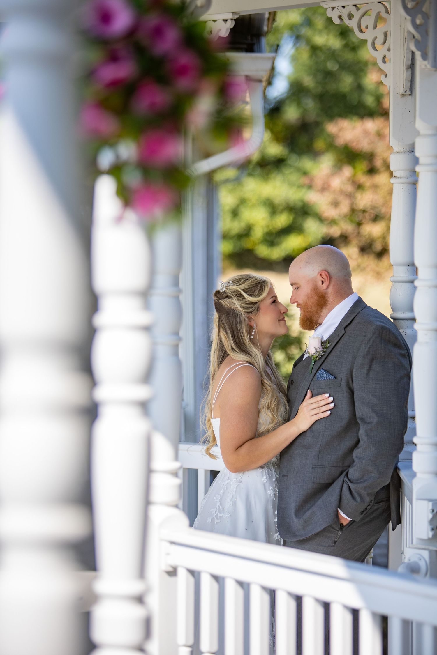Tender moment between newlyweds embracing on a white porch with pink flowers blooming in the foreground.