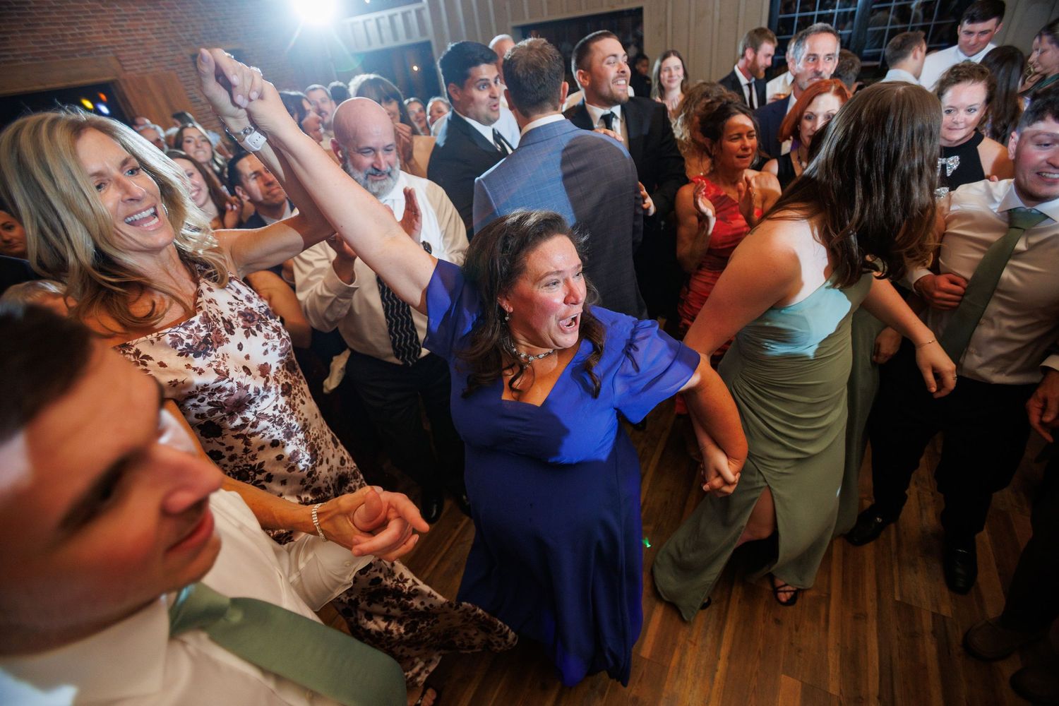 Joyful wedding guests dancing at lively reception, woman in blue dress celebrating.