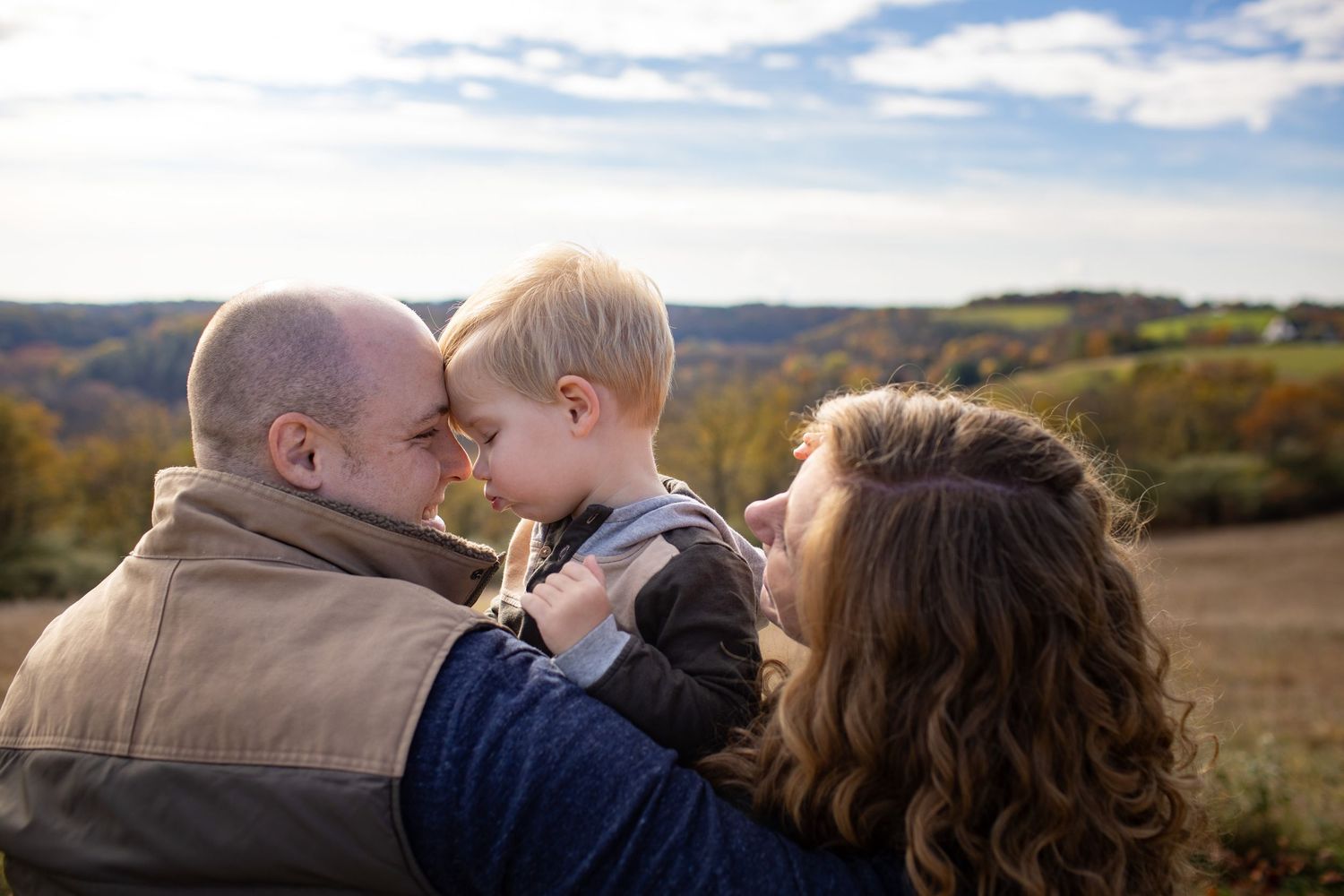 Couple sharing romantic kiss outdoors with scenic mountain landscape and autumn trees in background.