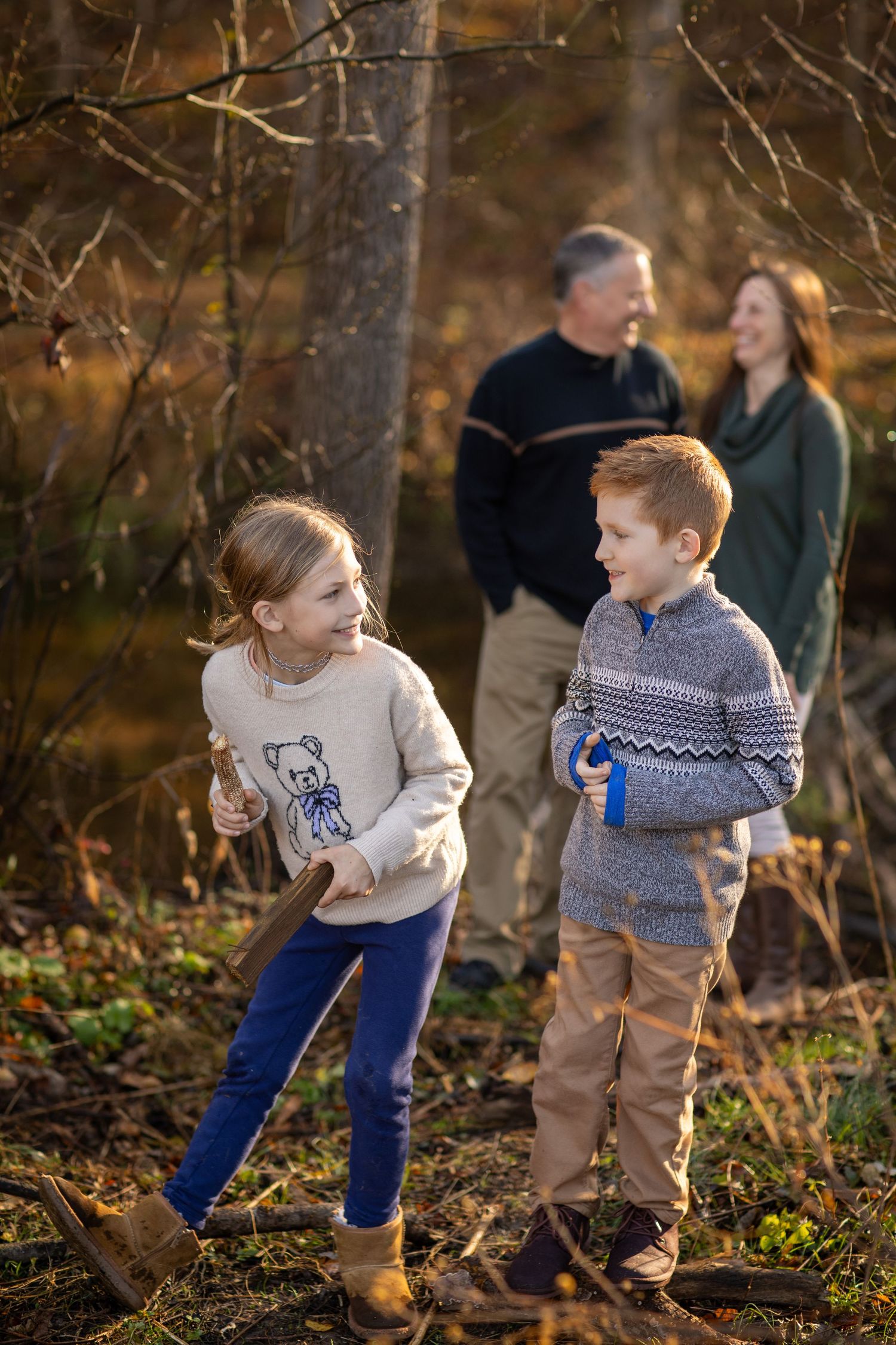 Children playing and exploring in a wooded area during autumn, wearing cozy sweaters.