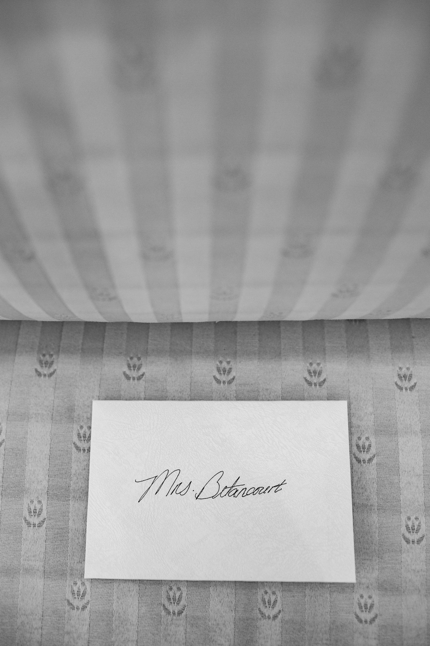 Black and white photo of a handwritten Mrs. Betancourt place card on a patterned tablecloth.