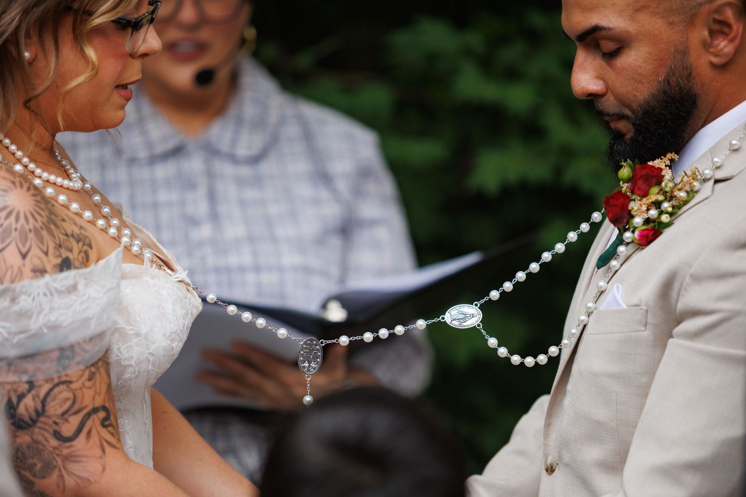 Close-up of bride and groom during ceremony with pearl lasso cord draped over their hands.