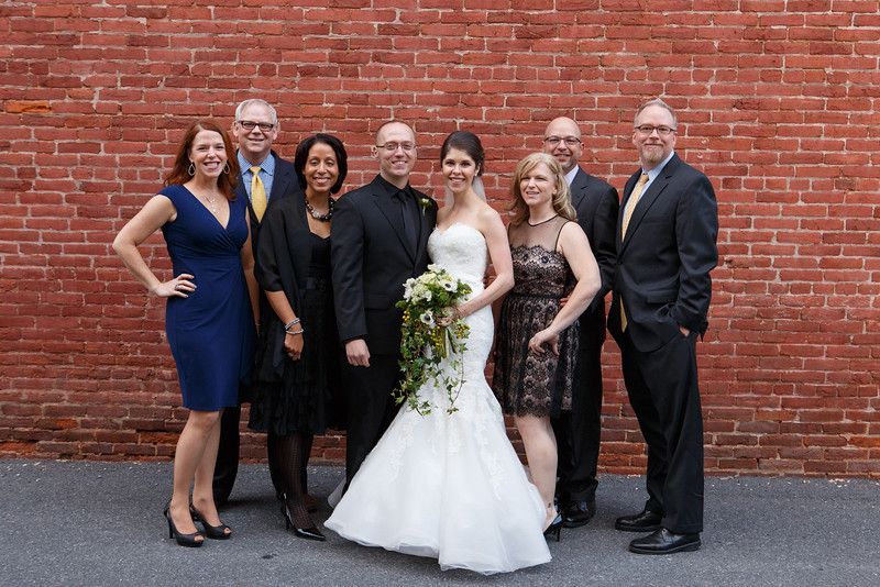 Wedding party members stand in front of rustic red brick wall at outdoor celebration venue during evening event.