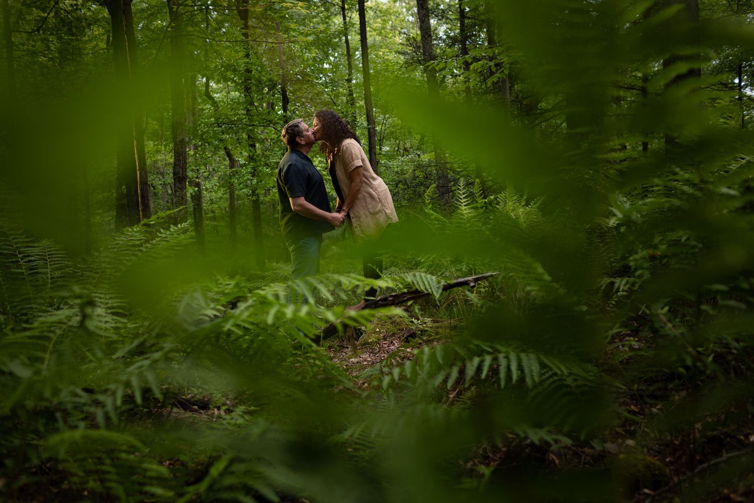 People sit among lush green ferns and trees in a serene woodland setting during a forest photoshoot.