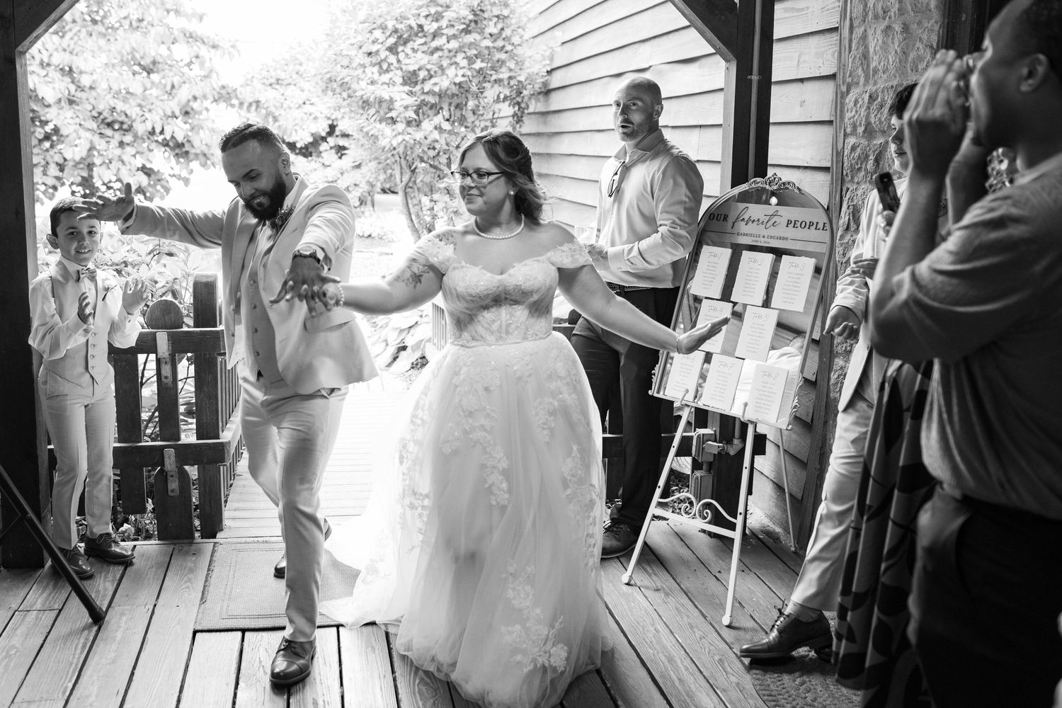 Bride and groom making grand entrance at rustic outdoor wedding reception in black and white.