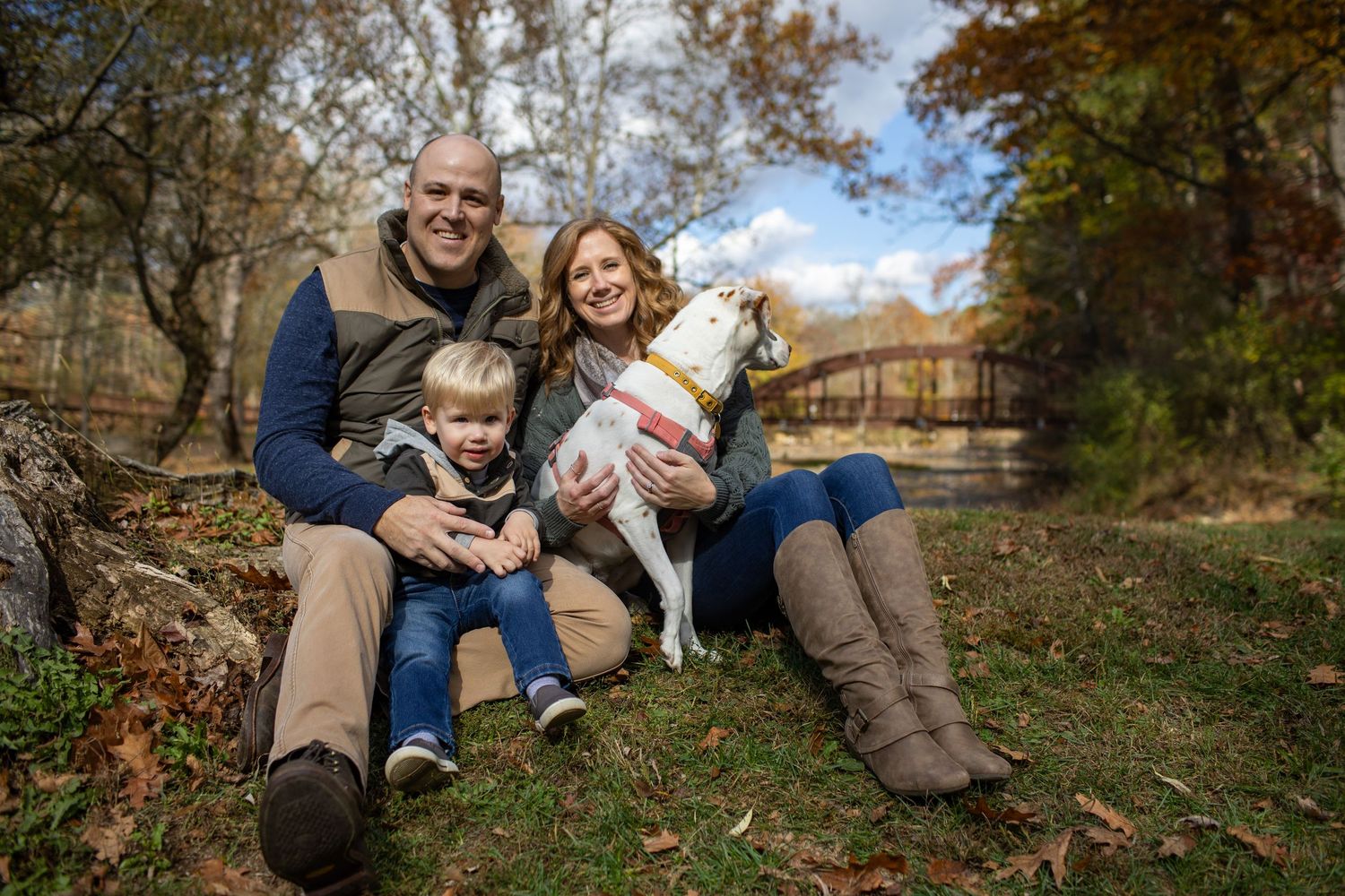 A couple and their child enjoy a playful autumn photoshoot on fallen leaves in a park setting.
