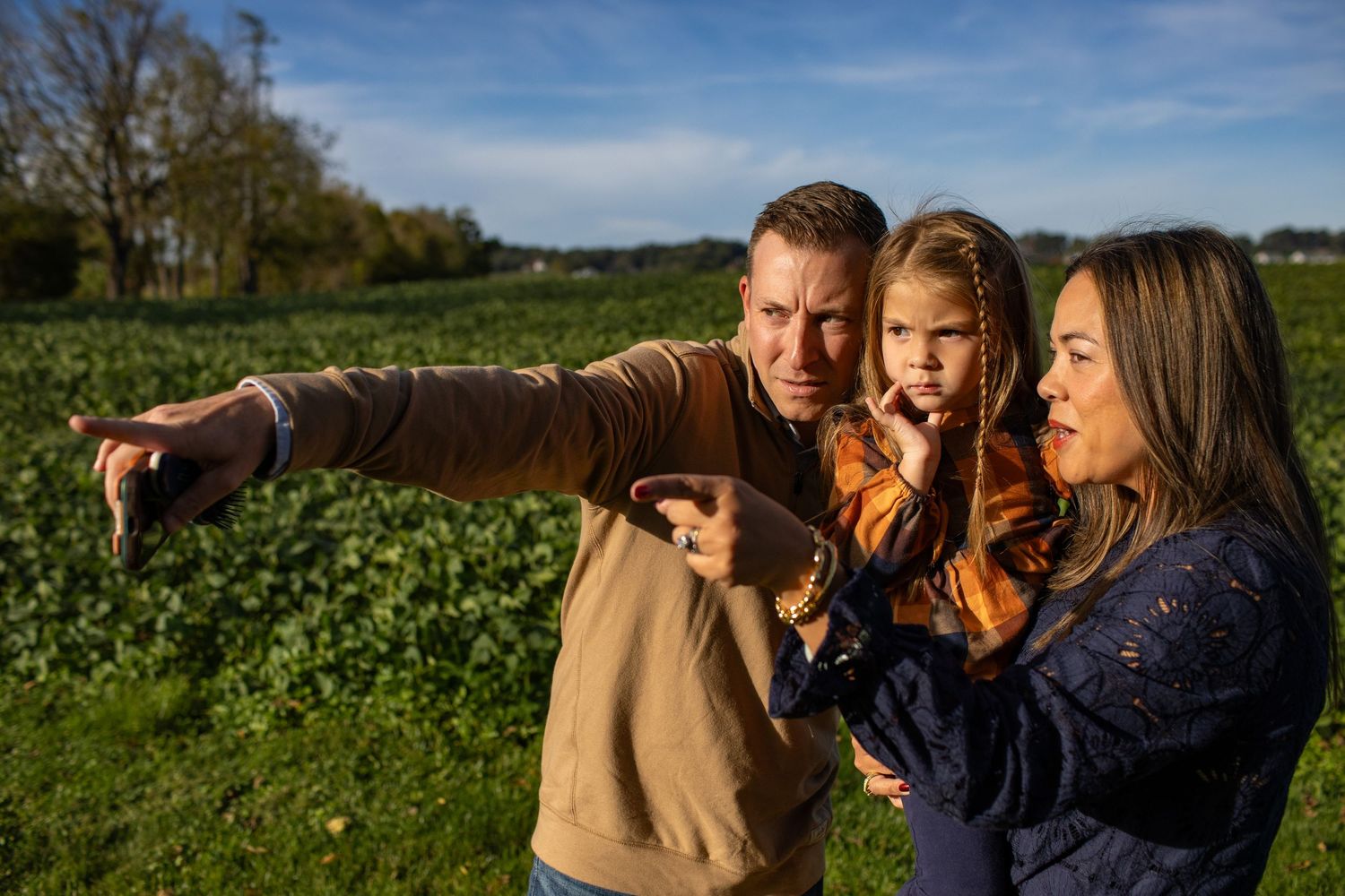 A family shares a joyful moment outdoors while pointing at something in the distance on a sunny day.