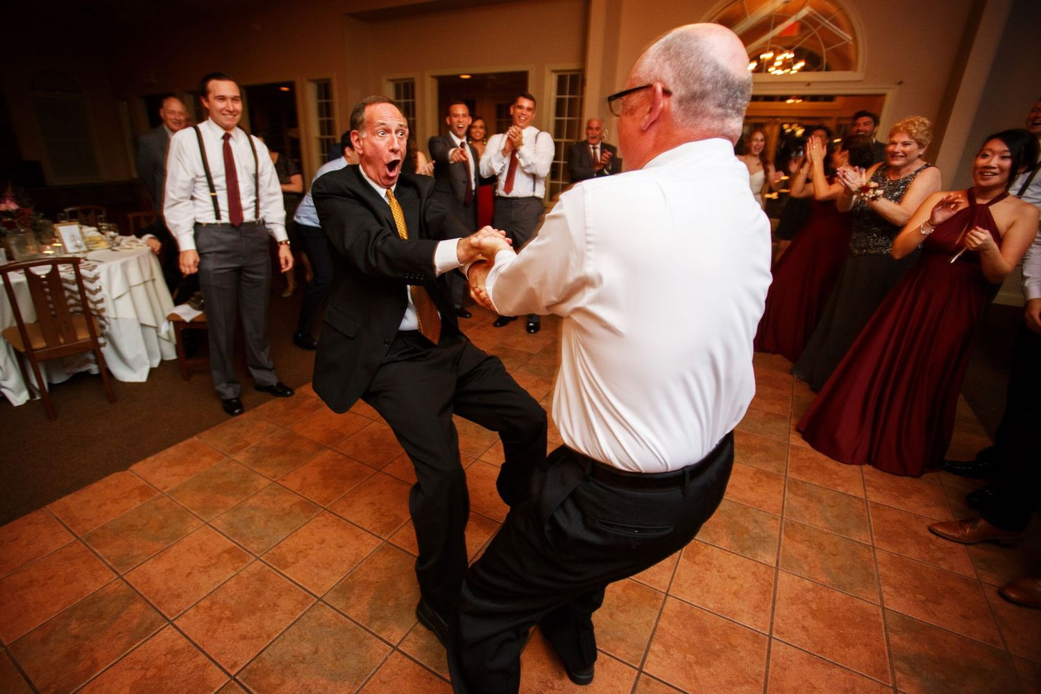 Two men in formal wear dancing and enjoying themselves on a tile dance floor at an event.