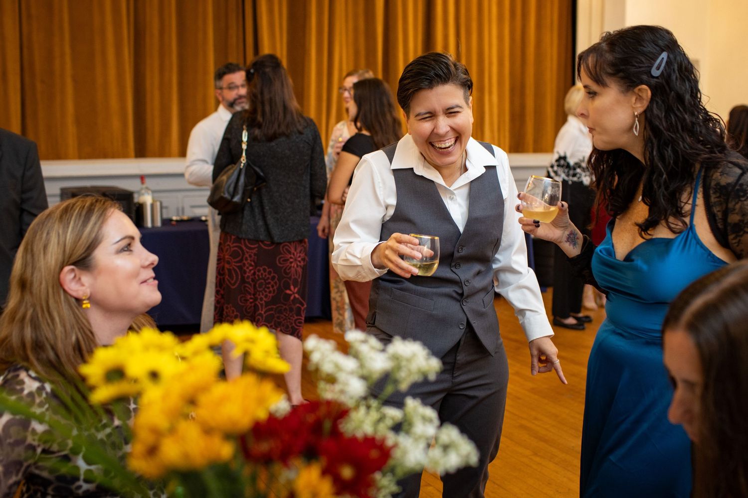 Wedding guests mingle and socialize at an elegant reception with yellow and white floral centerpieces on tables.