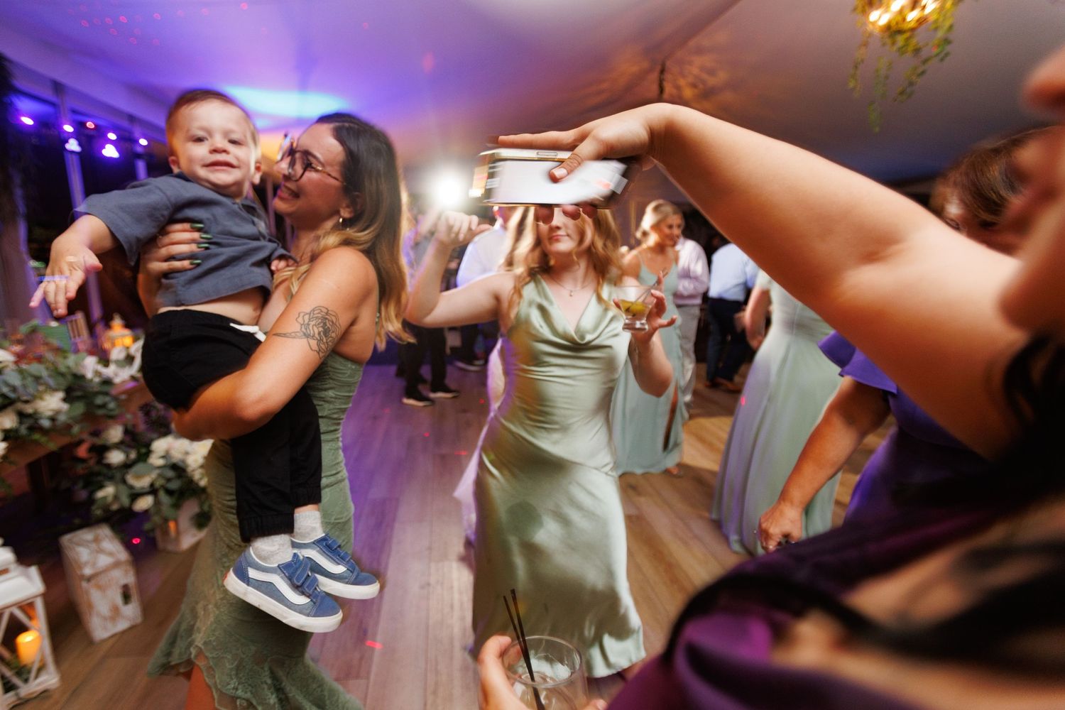 Wedding reception guests dance enthusiastically on a purple-lit dance floor during an energetic celebration.