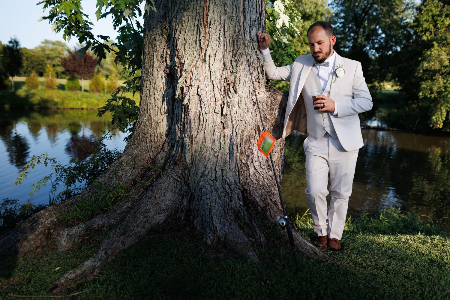 Professional wedding photography session in a scenic park setting near water and large trees during golden hour.