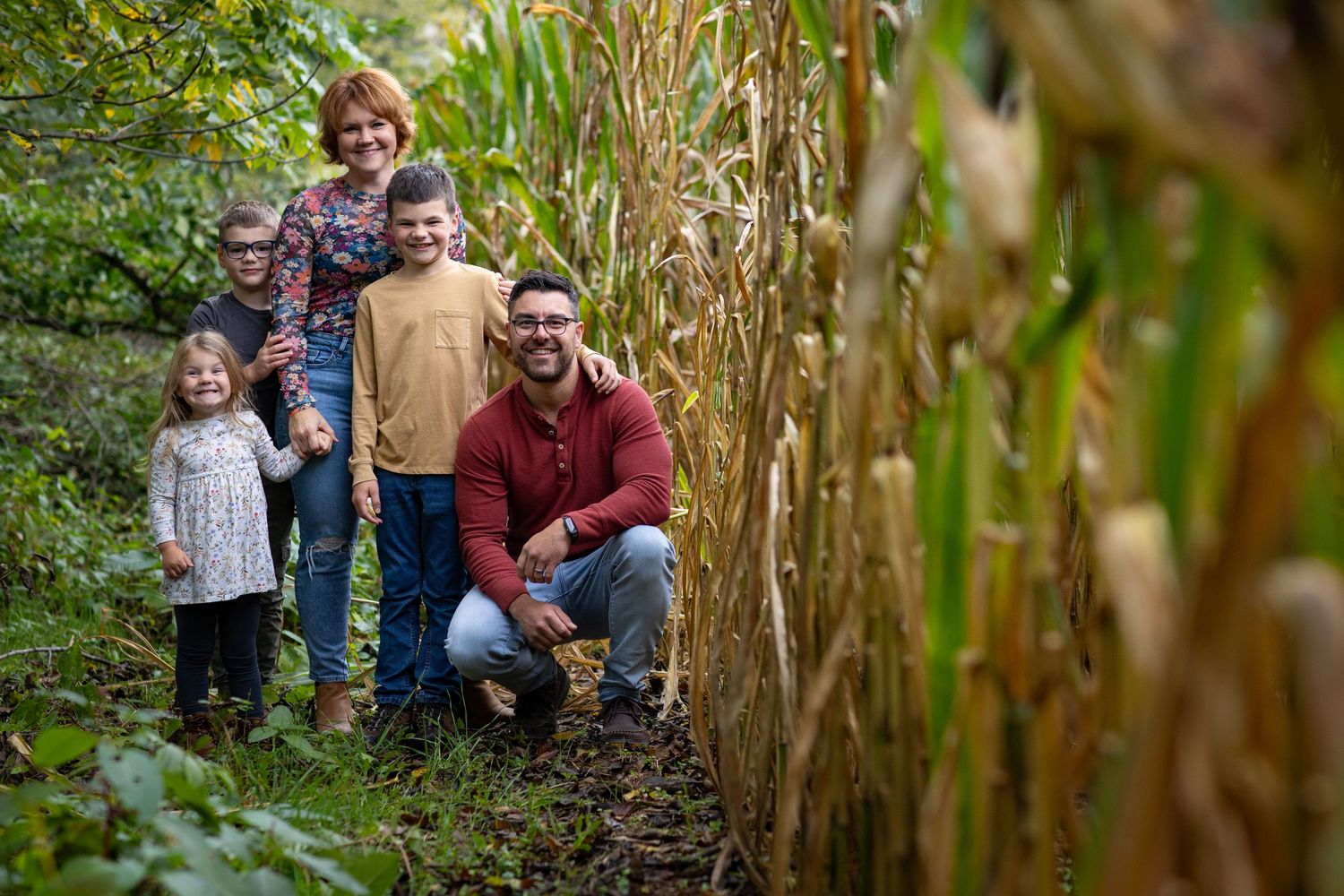 Family enjoying a fall photoshoot among green and yellow foliage in a natural outdoor setting.