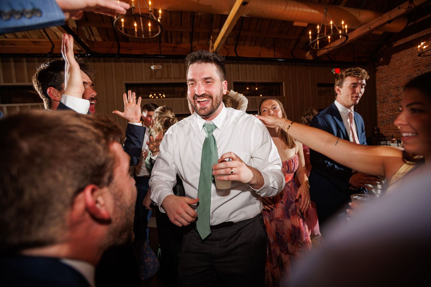 Smiling man in white shirt and green tie celebrates joyfully on the wedding reception dance floor.