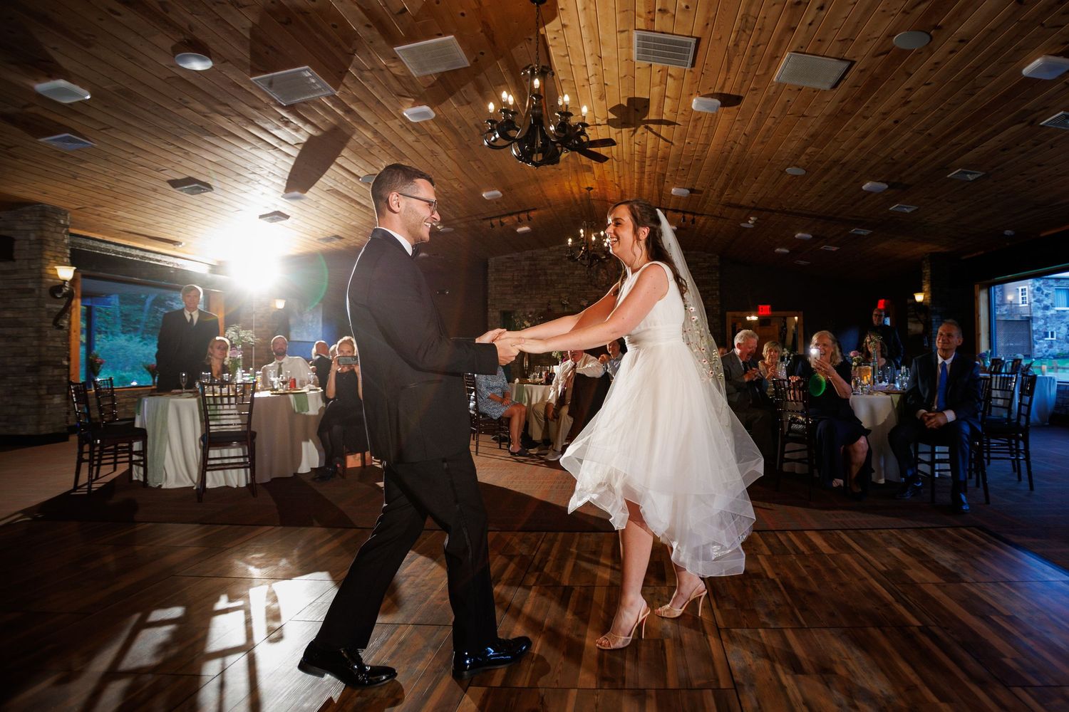 Bride and groom sharing energetic first dance in rustic wood-paneled wedding reception venue.