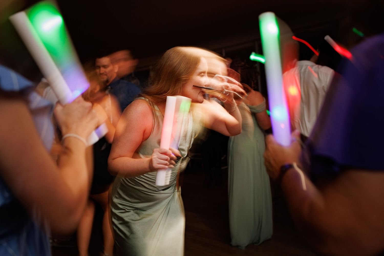 People dance at a nightclub while holding colorful glowing LED foam sticks during a party celebration.