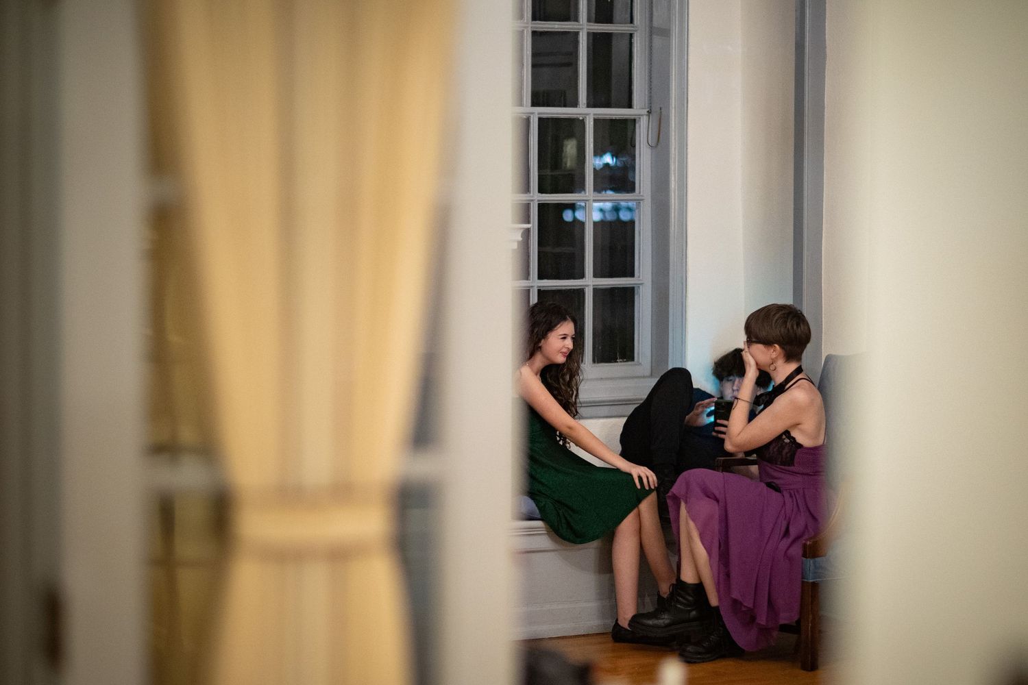 Silhouetted figures by window in elegant room during evening gathering.