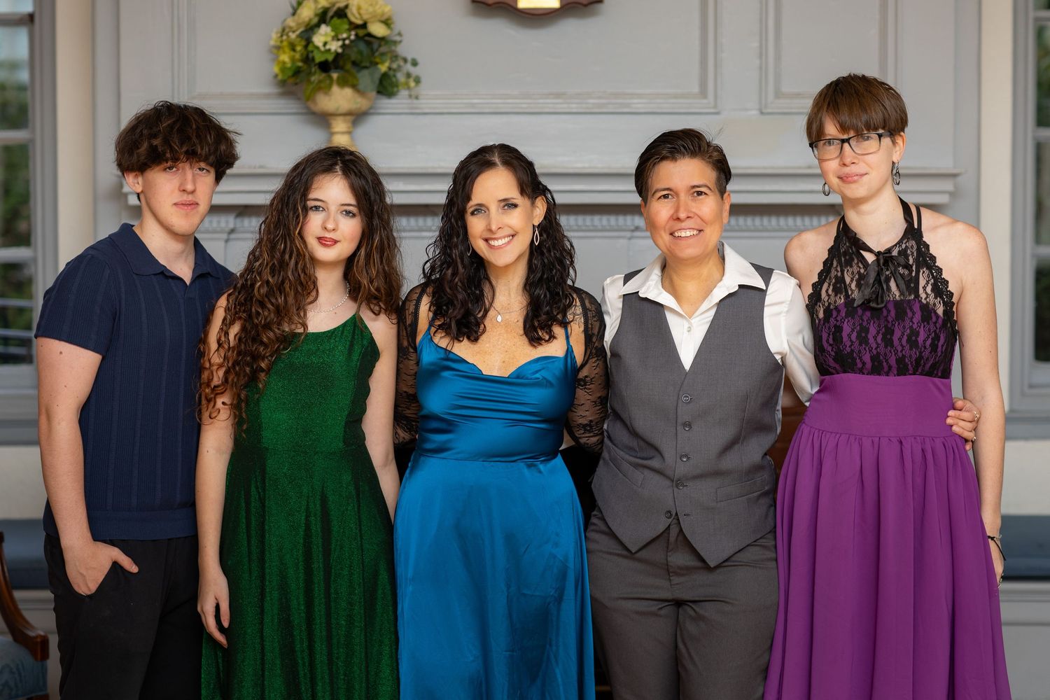 A group of five people dressed in formal attire including navy, green, blue, grey, and purple outfits standing together.