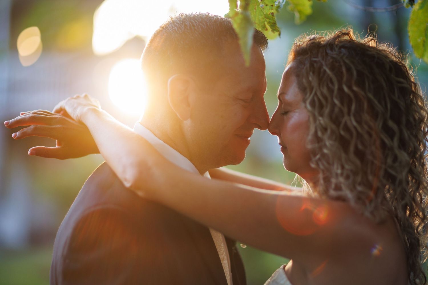 Bride and groom share an intimate moment bathed in warm golden sunset light outdoors.