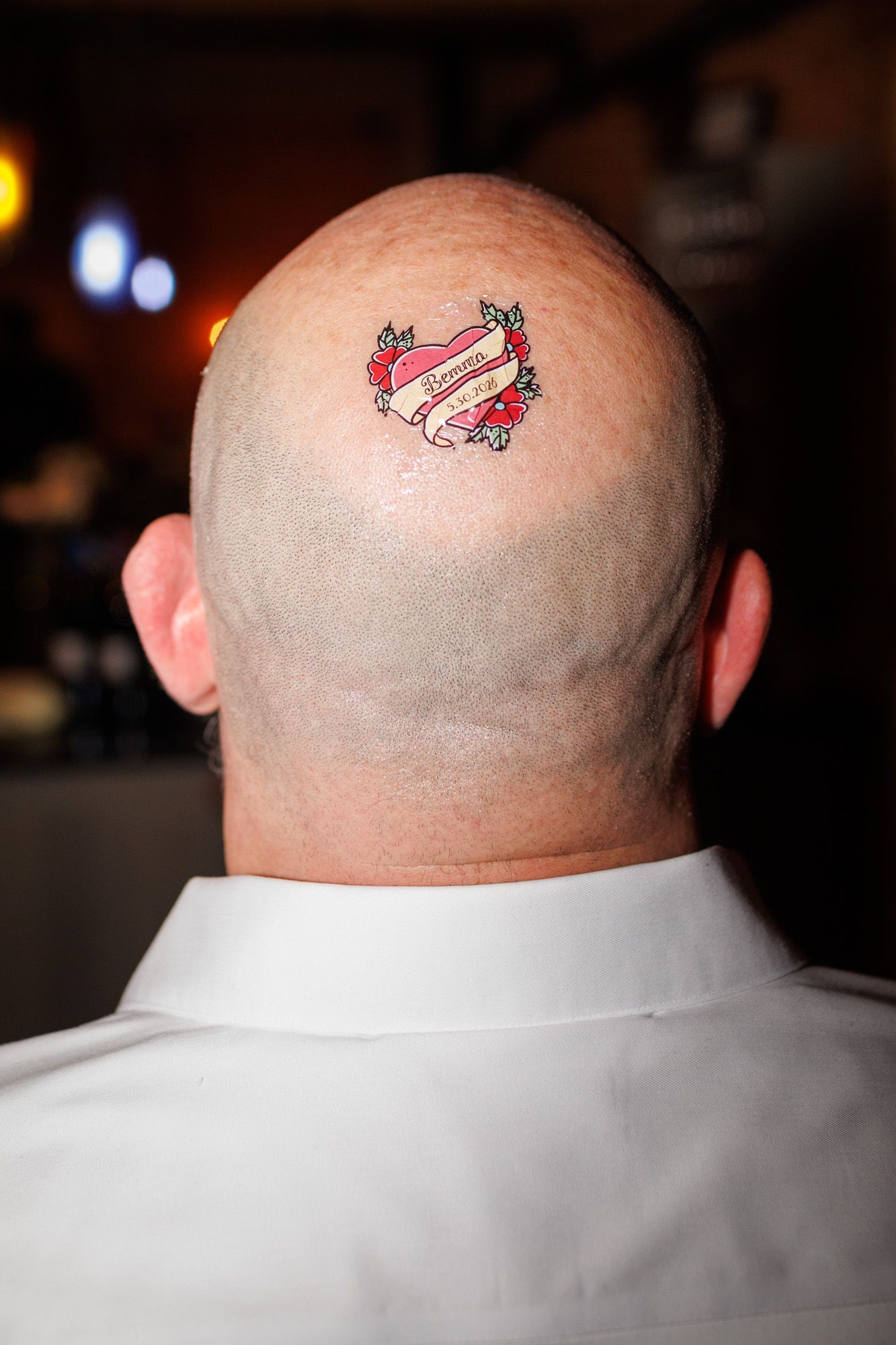 Bald man with a decorative heart tattoo on the back of his head at an event.
