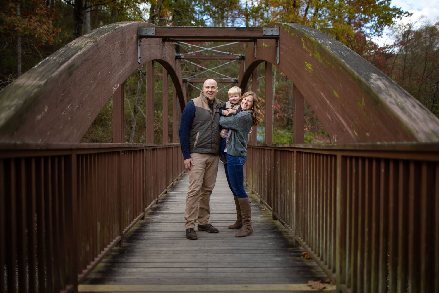 People standing on a wooden boardwalk surrounded by autumn trees in a romantic outdoor setting.