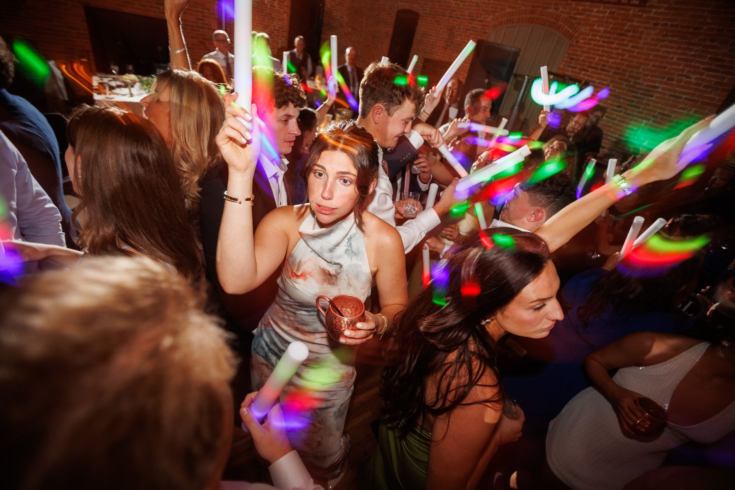 Crowd of party guests dancing with colorful glow sticks at energetic nightclub event.