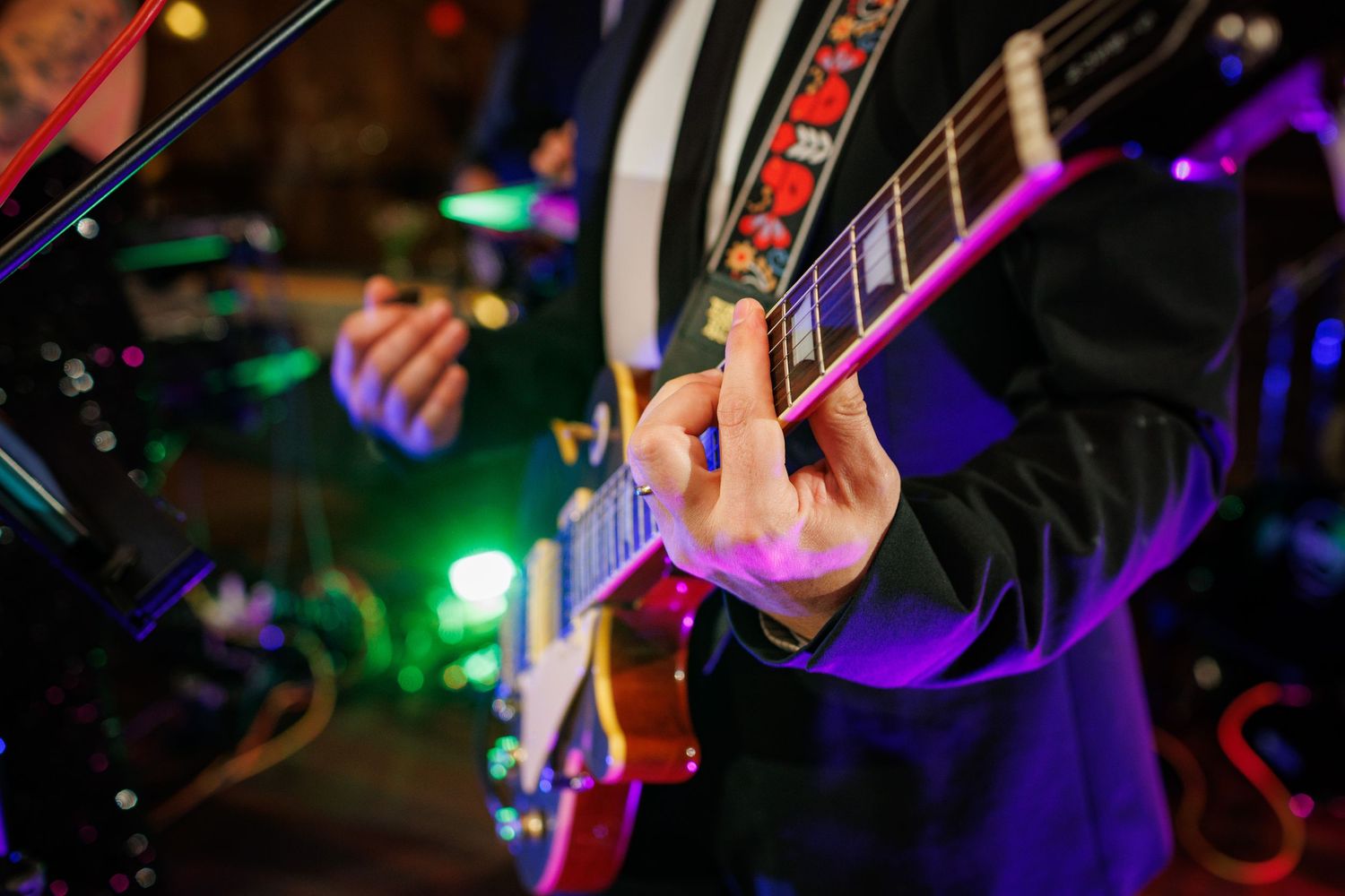 Close-up of guitarist playing electric guitar with colorful stage lights at wedding reception.