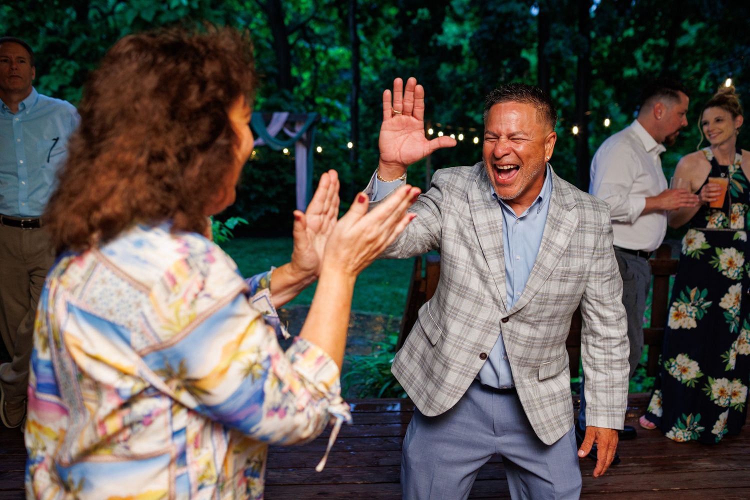 Wedding guest in plaid blazer enthusiastically dancing with another guest at an outdoor reception.