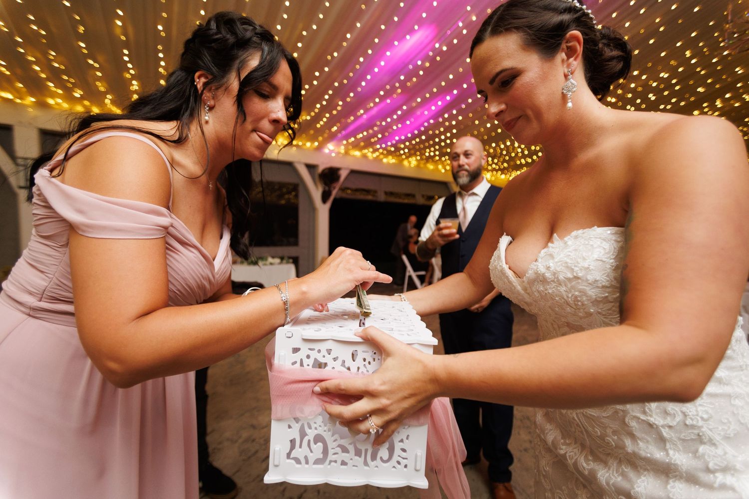 Wedding reception scene with string lights and pink lighting creating a festive dance floor atmosphere.